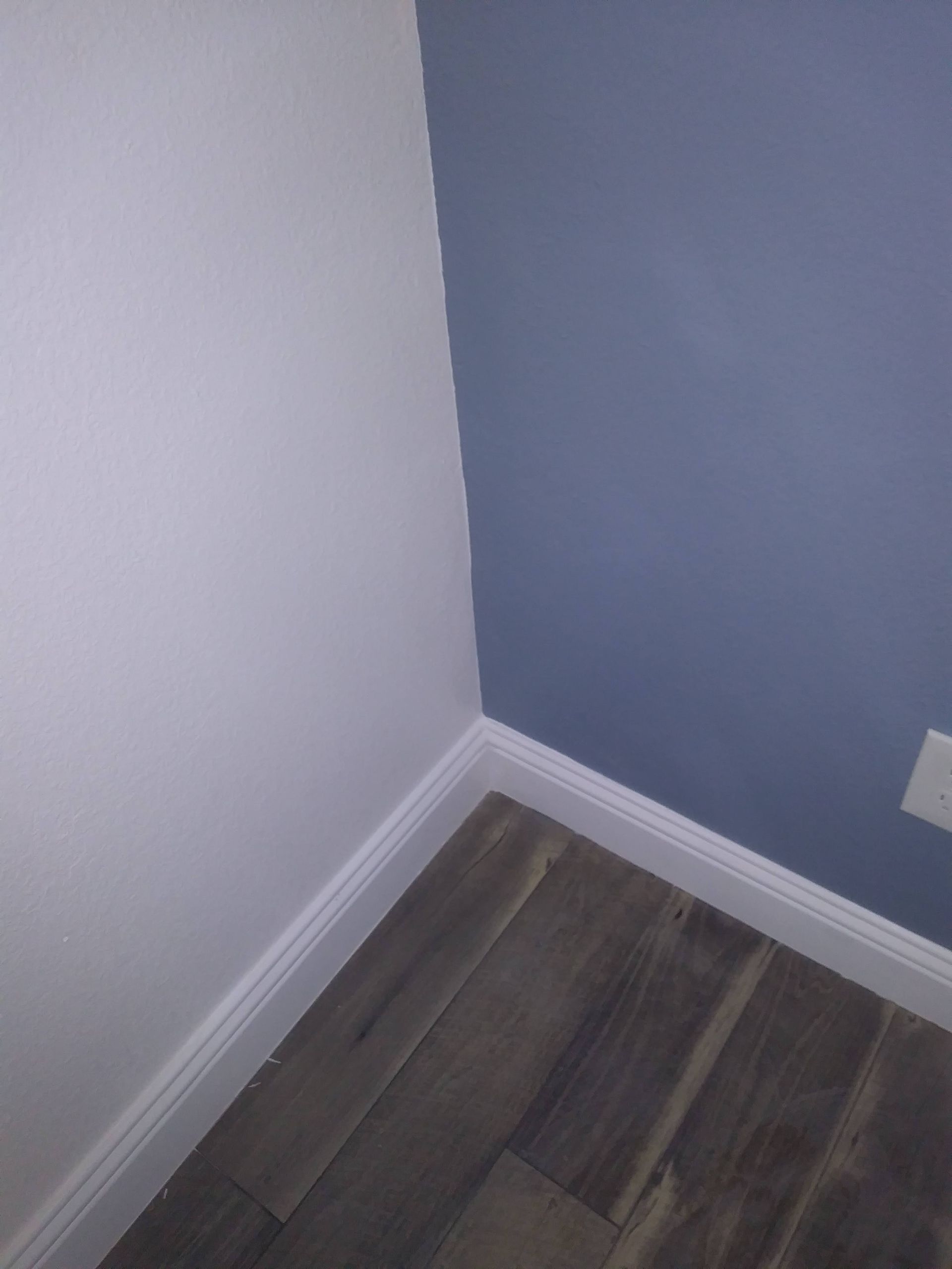 Empty corner of a room with white and blue walls, white baseboards, and wood flooring.