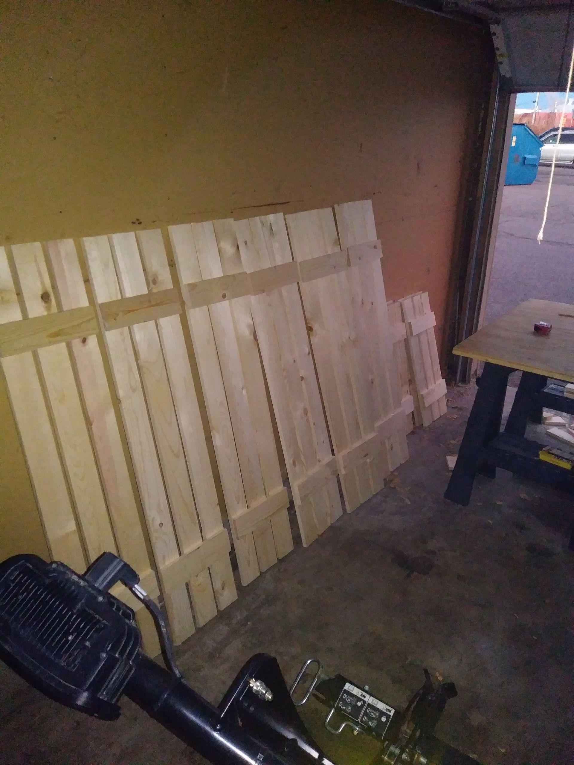 Wooden slats leaning against a wall in a dim indoor space, with a fan and table in the foreground.