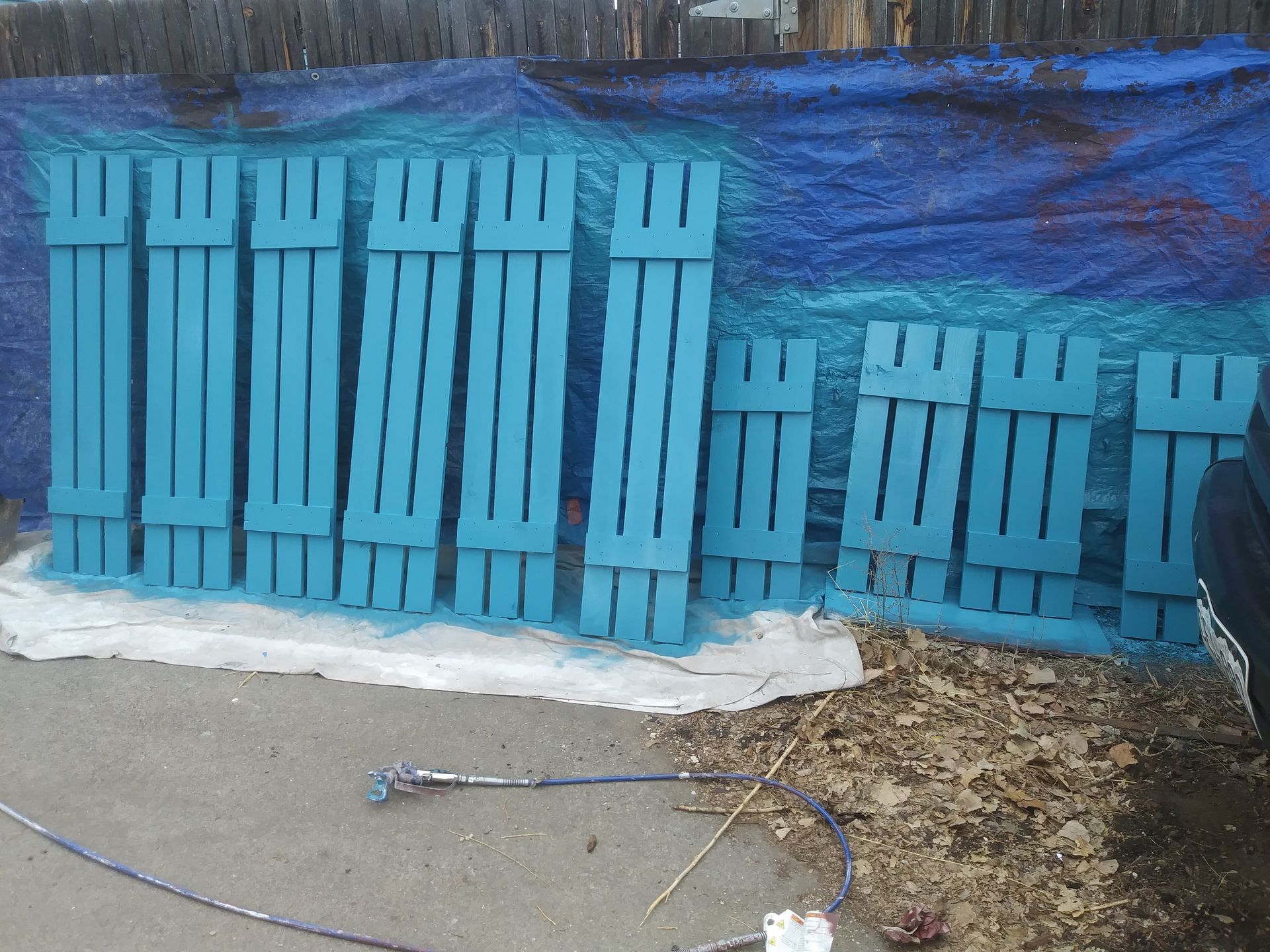 Blue wooden pallets lined up against a blue tarp, with snow on the ground and a rope in front.