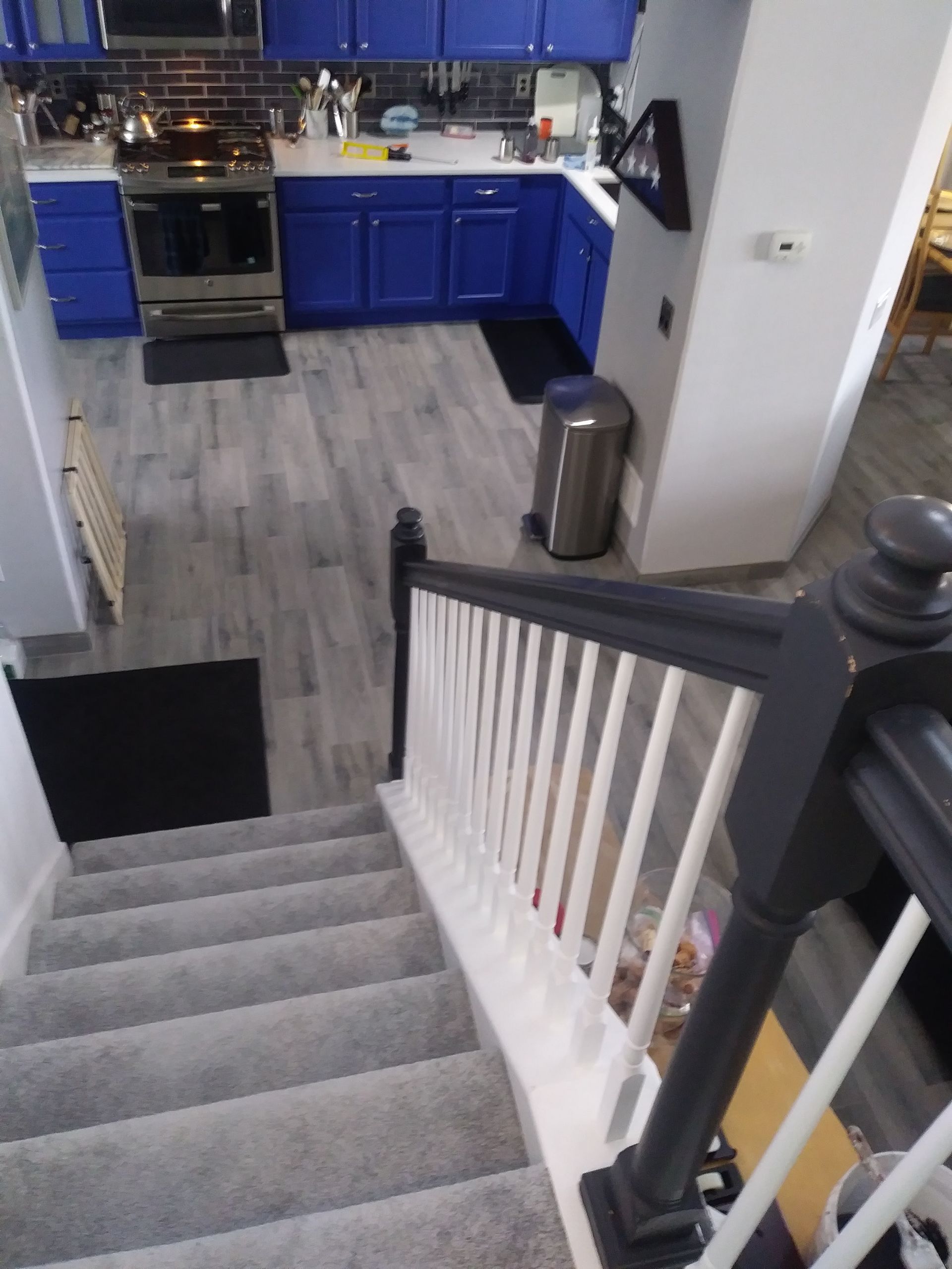 Staircase overlooking a blue kitchen with gray floors and a stainless trash can by the wall.