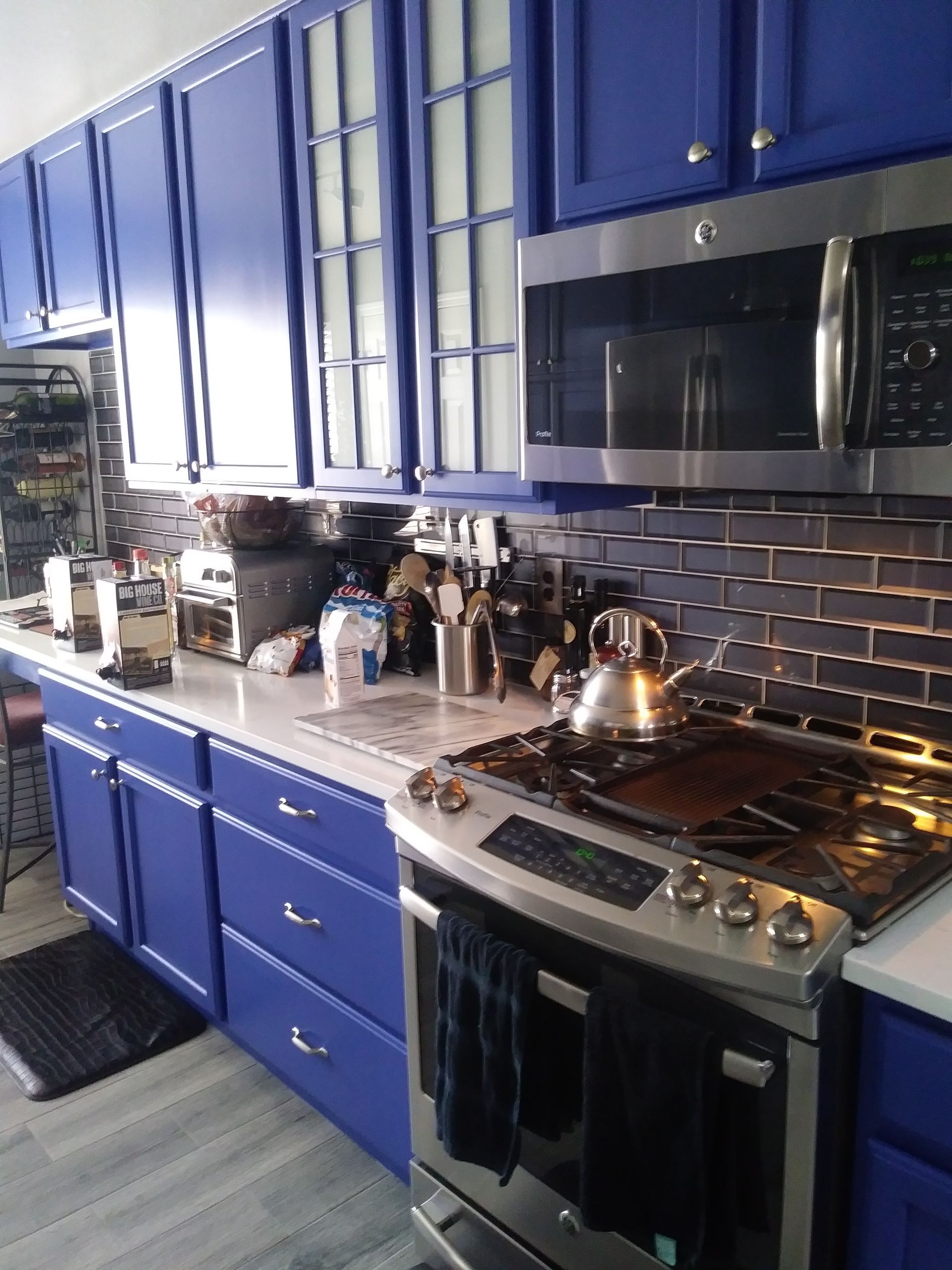 Blue-and-white kitchen with stainless stove, microwave, and countertop items by large windows