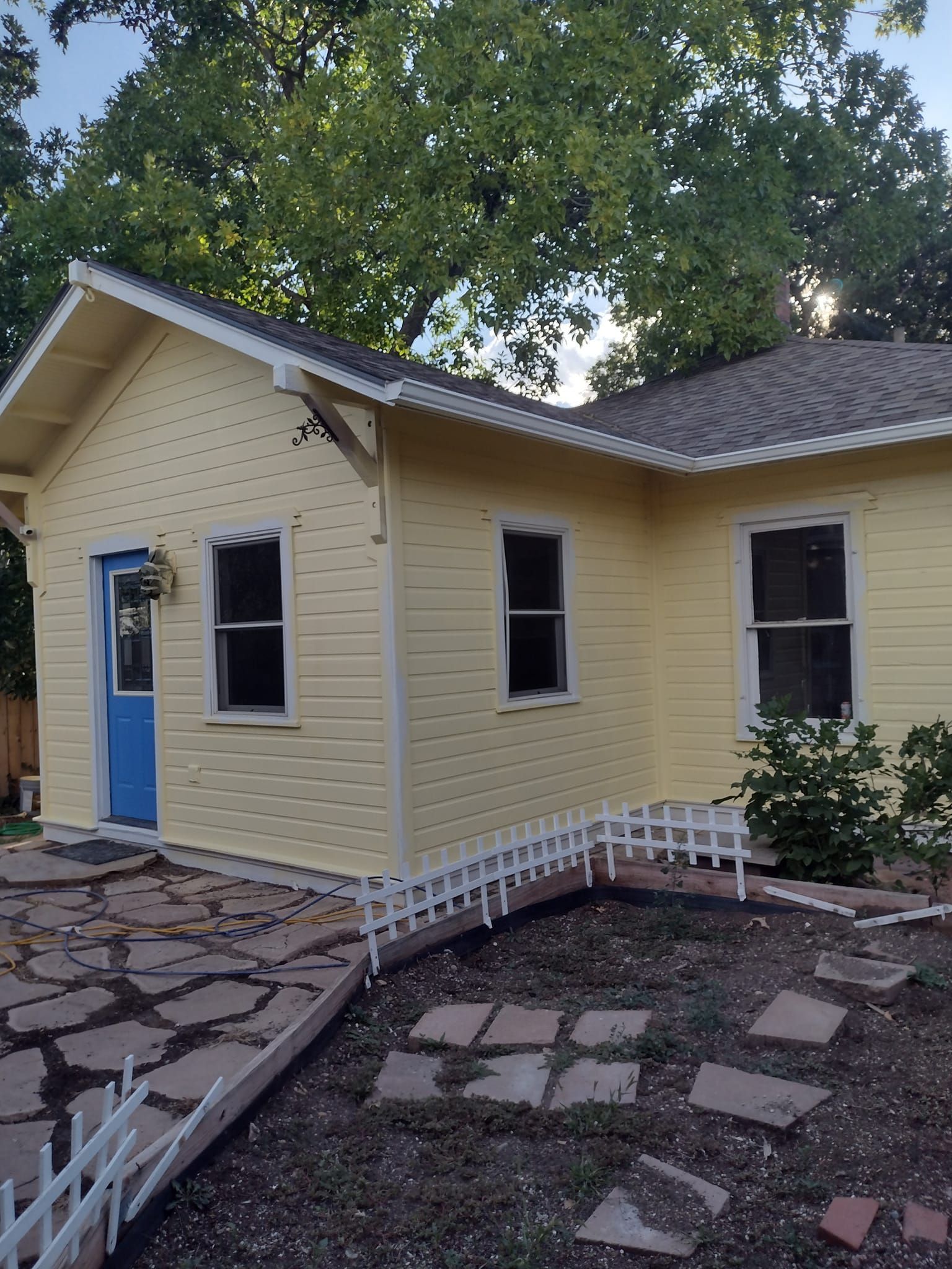 A light yellow house with a blue door and white trim, featuring a decorative fence in the yard.
