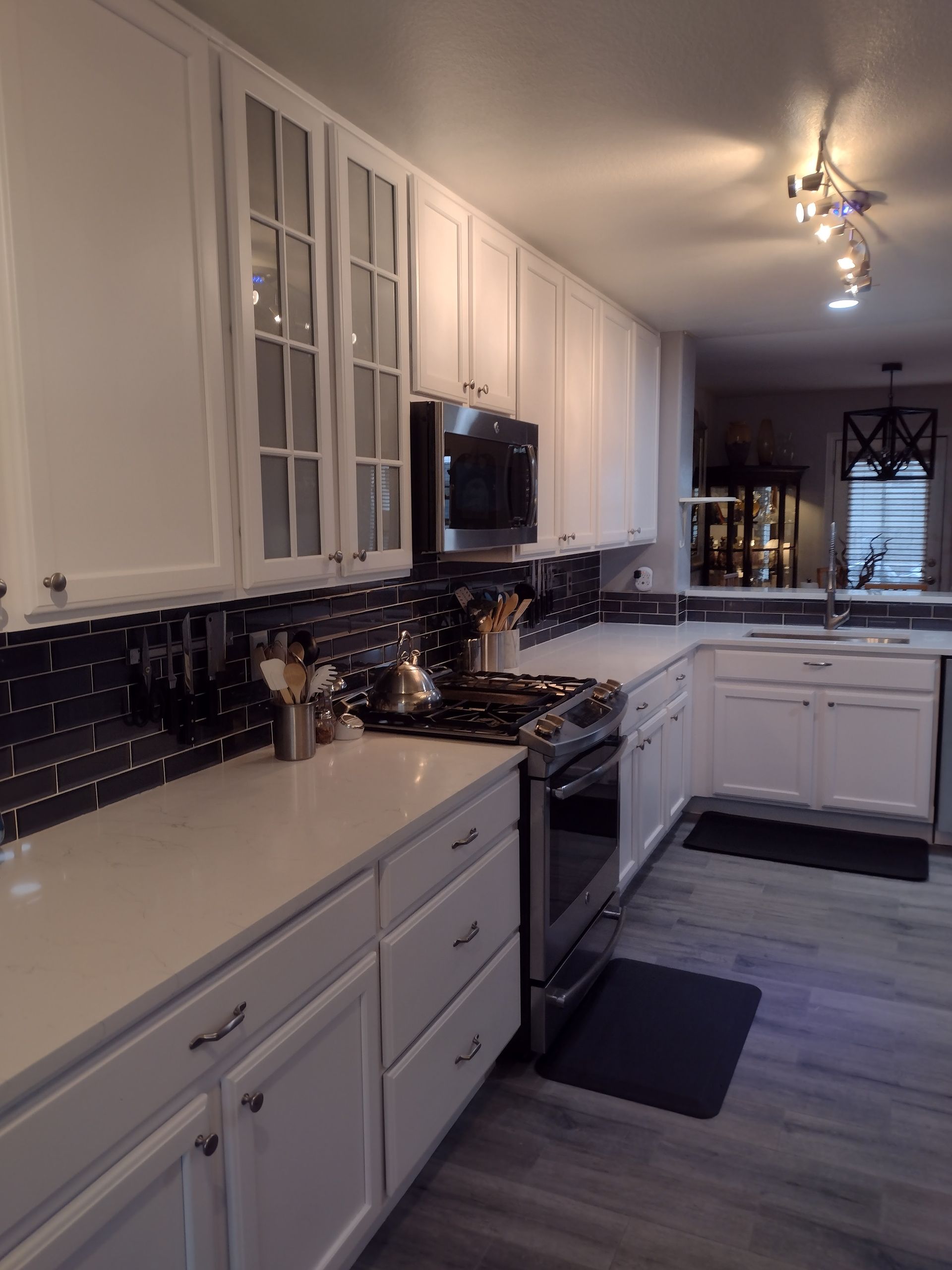 Modern white kitchen with black countertops, glass-front cabinets, and pendant lights.