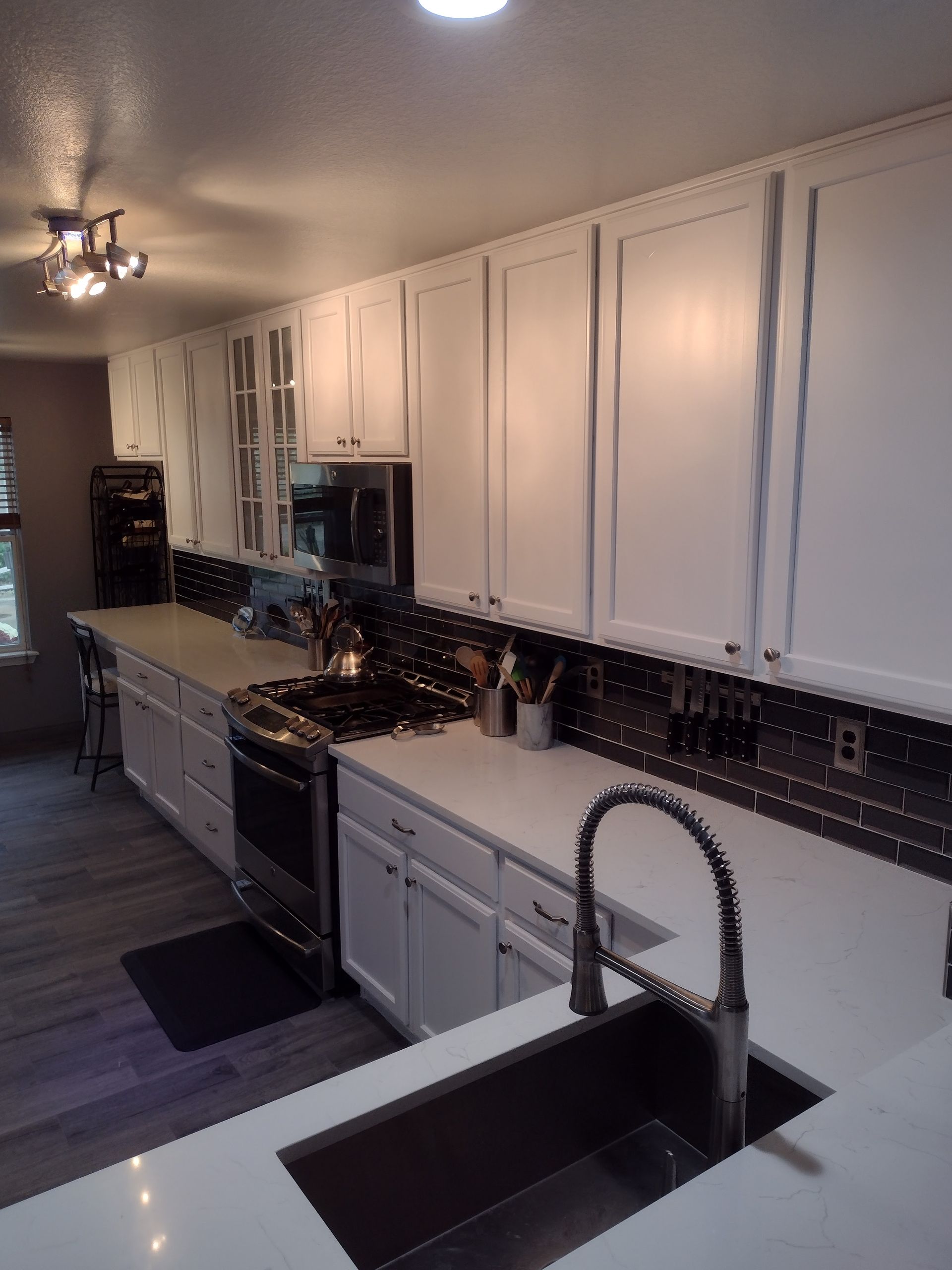 Bright kitchen with white cabinets, black countertops, and a deep sink in the foreground.