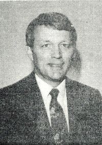 Black-and-white portrait of a man in a suit and tie, facing the camera with a slight smile.
