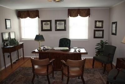 Home office with wooden desk, two chairs, green lamp, and framed art on cream walls