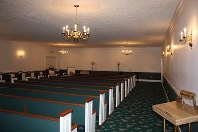 Empty church chapel with rows of pews, green carpet, and chandeliers under warm lighting