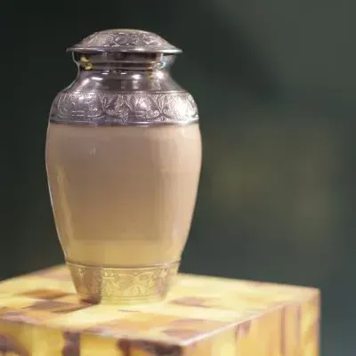 Silver lidded jar with a cloudy liquid, sitting on a yellow patterned box against a blurred background