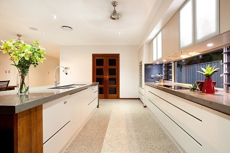 A Long Kitchen with White Cabinets and A Ceiling Fan — Custom Cabinets Design in Berrimah, NT