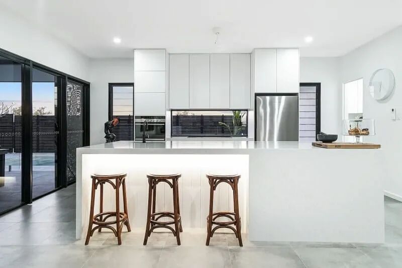 A Kitchen With White Cabinets and Stools and a Large Island — Custom Cabinets Design in Berrimah, NT