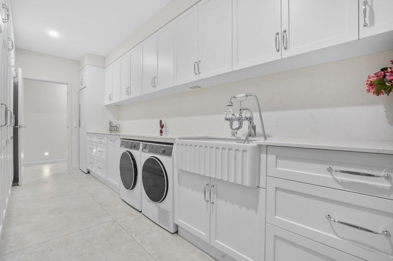 A Laundry Room With White Cabinets, a Washer, and Dryer — Custom Cabinets Design in Berrimah, NT