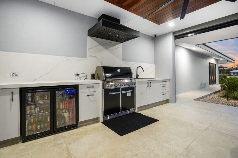 An outdoor kitchen with barbecue, sink and bar fridges  — Custom Cabinets Design in Berrimah, NT