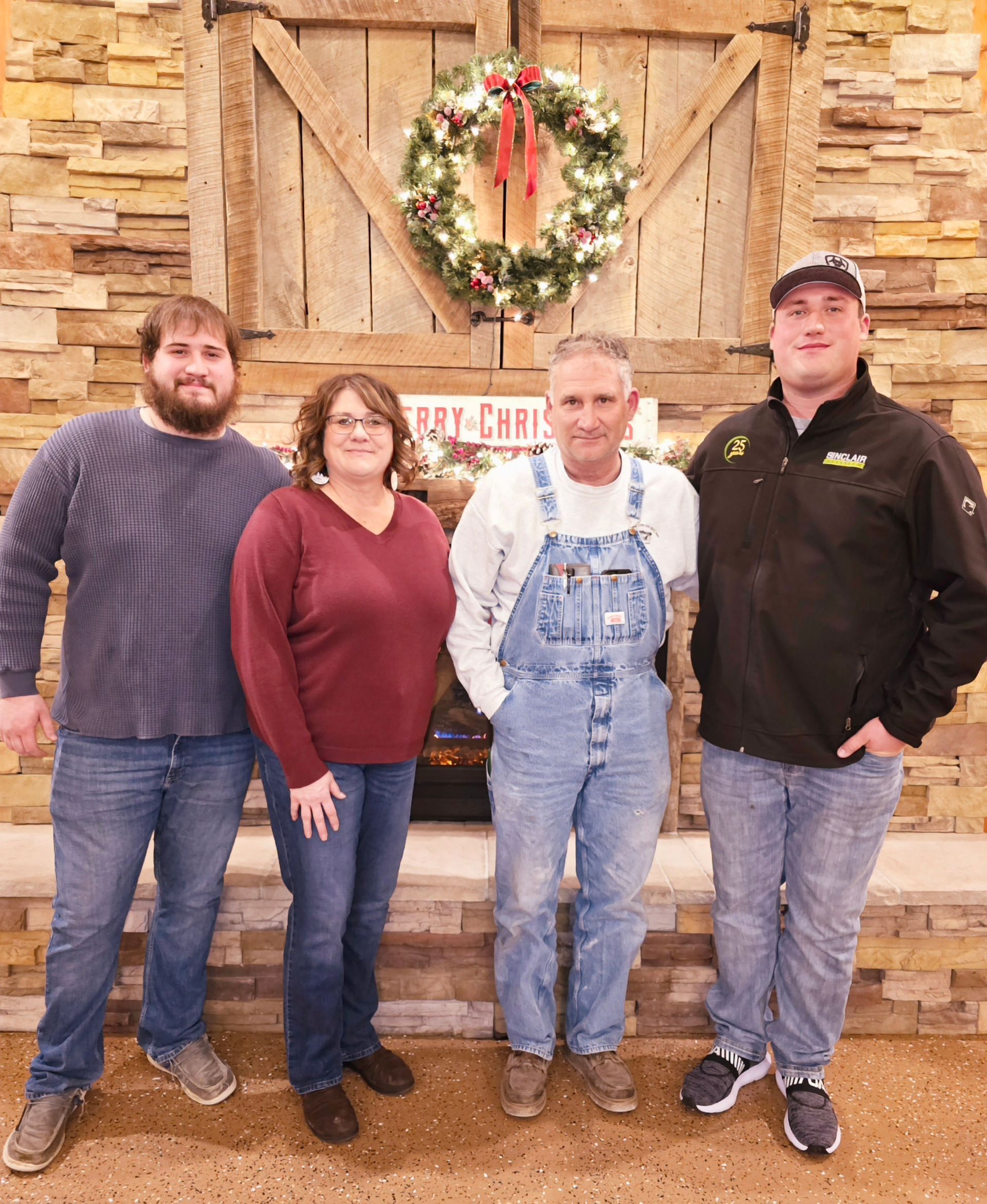 Four people standing indoors in front of a stone wall with a holiday wreath, posing for a photo.