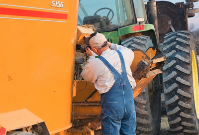 Man working on an orange farm machine beside a large tractor tire