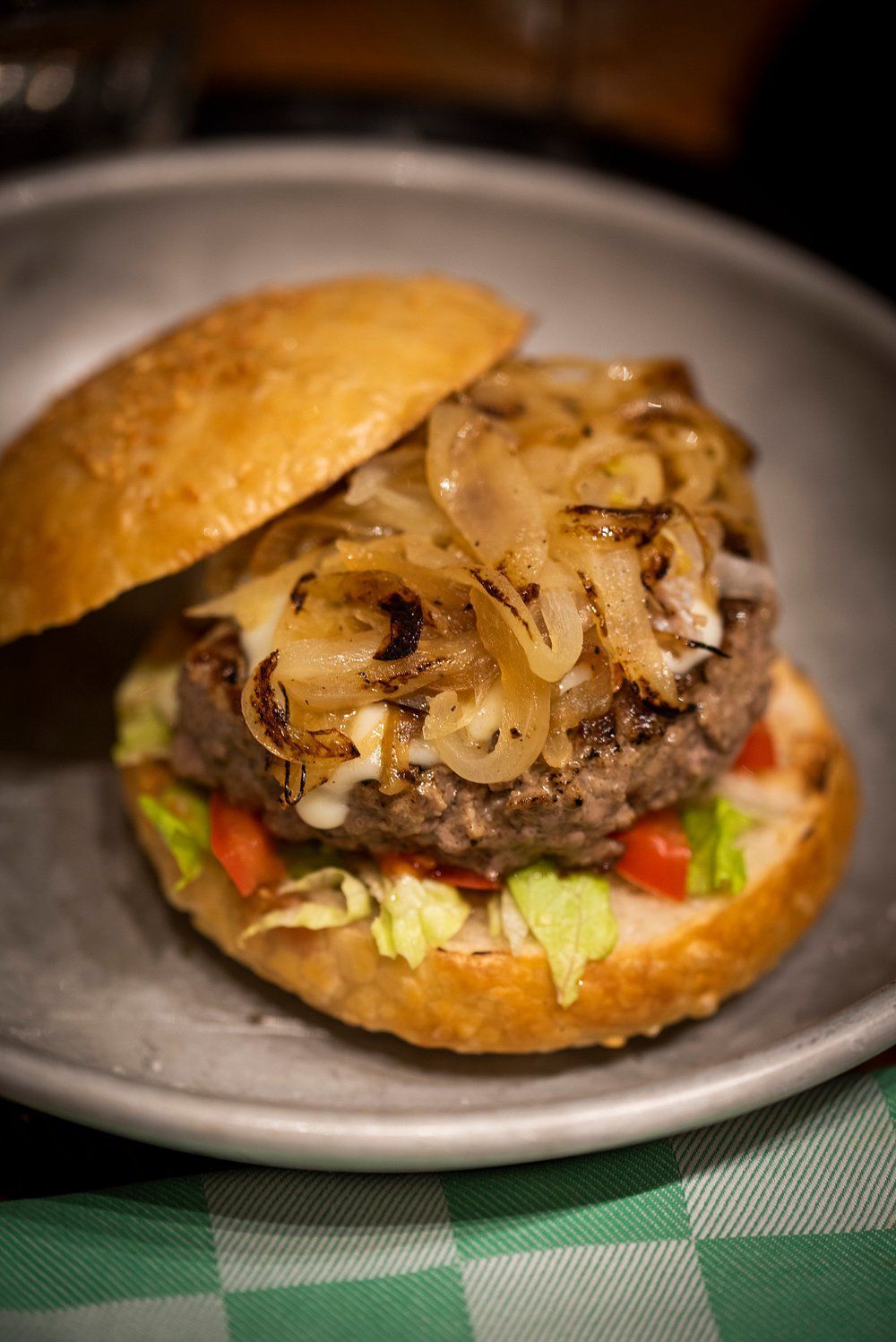 Hamburger con cipolle caramellate, formaggio, lattuga e pomodoro, servito in un panino e in una ciotola di metallo.