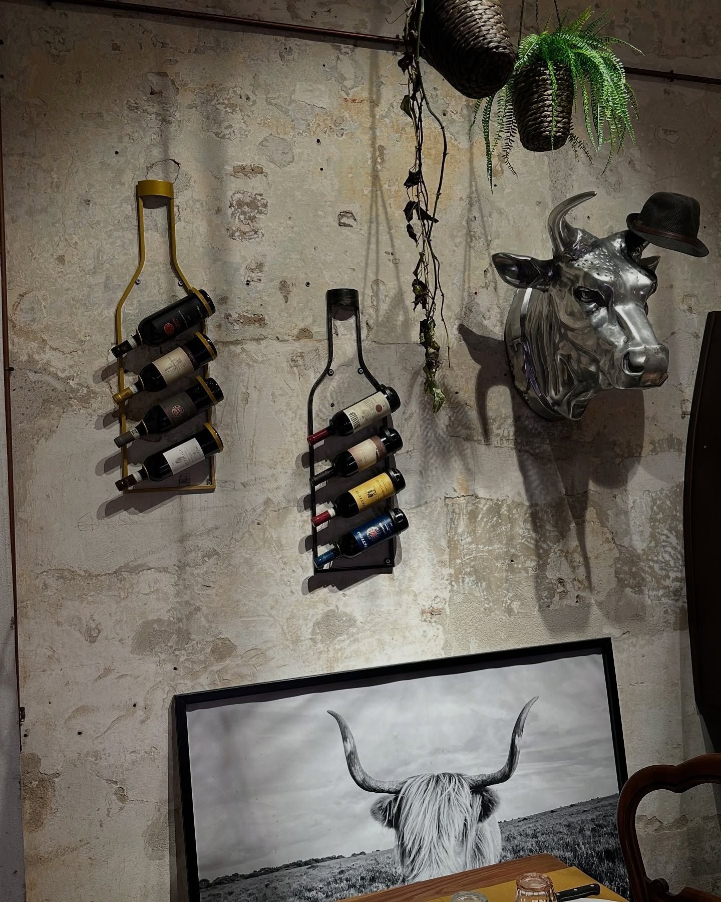 Portabottiglie a forma di bottiglia di vino su una parete strutturata, con una scultura a forma di testa di mucca e una foto di mucca incorniciata.