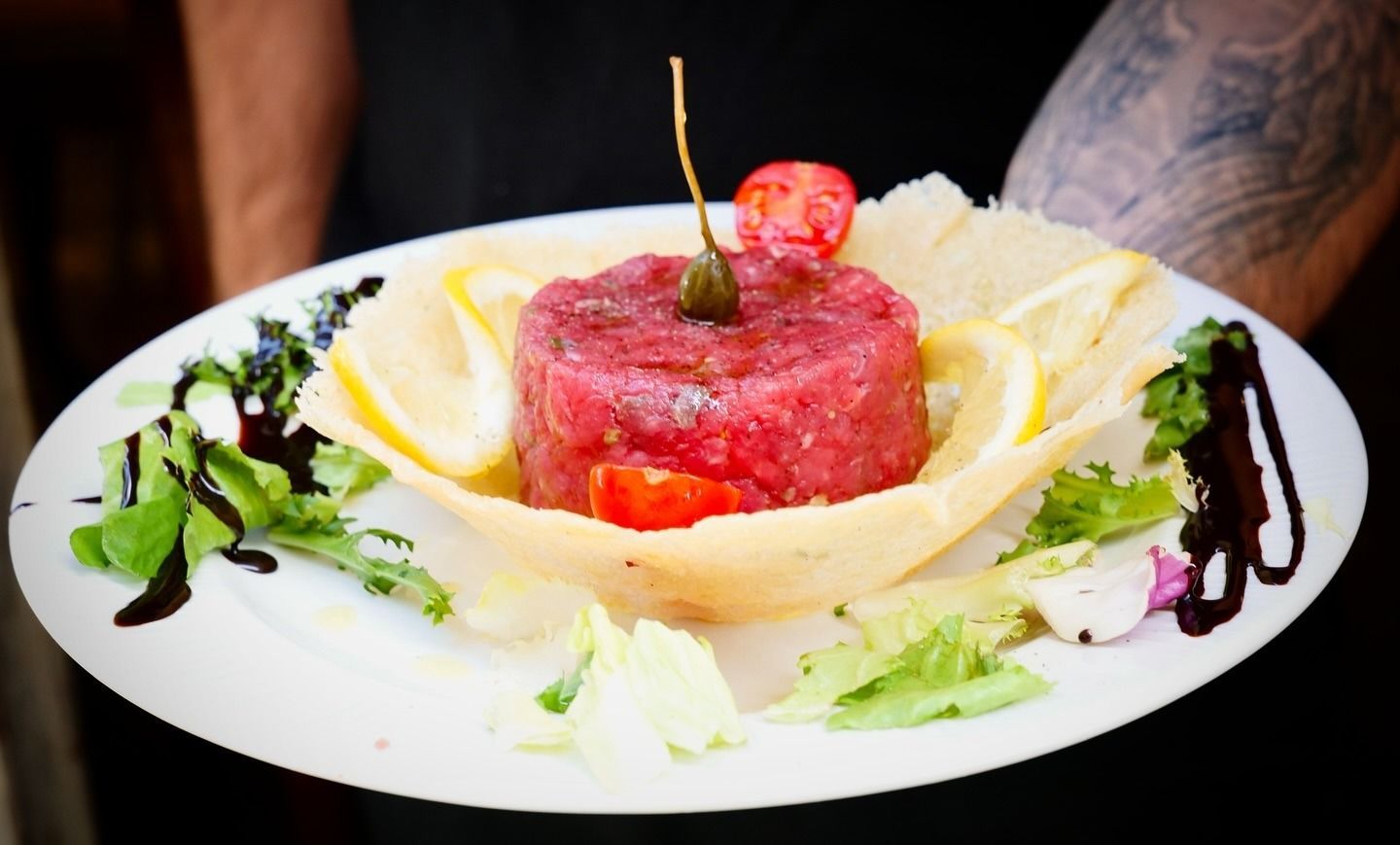 Piatto di tartare di manzo, guarnito con limone, verdure e glassa balsamica.