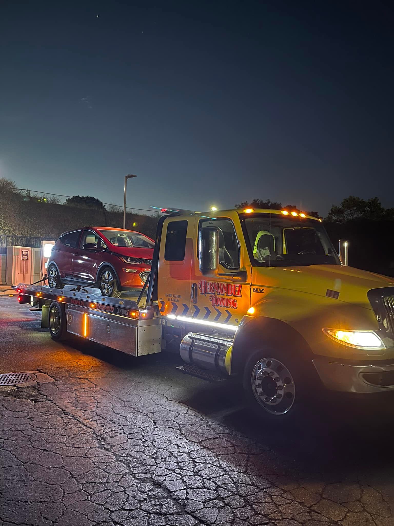 Tow truck at night transporting a red car. Yellow truck has lights on, dark sky. Tow truck at night transporting a red car. Yellow truck has lights on, dark sky.