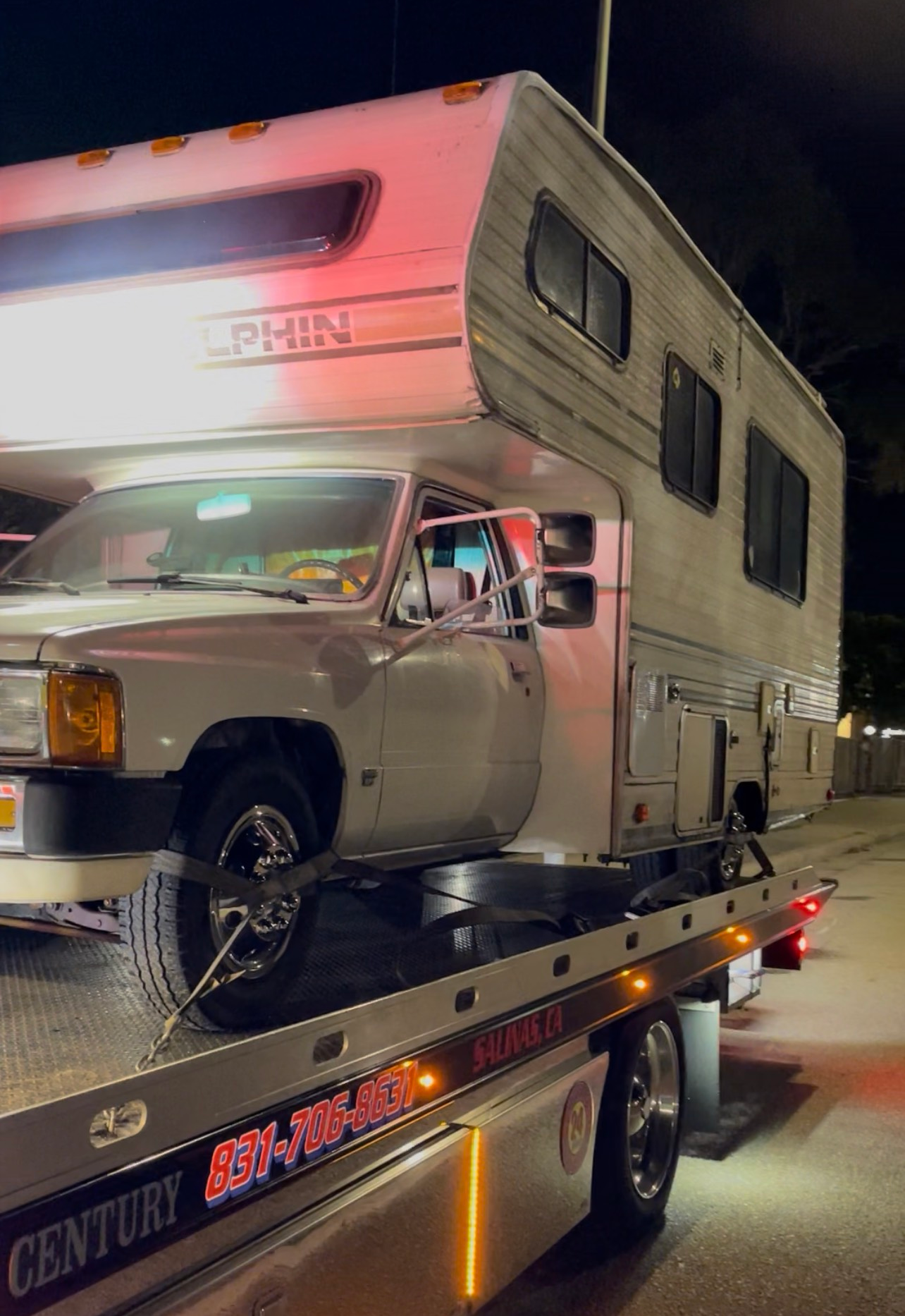 A white van with front-end damage being loaded onto a tow truck on a road.