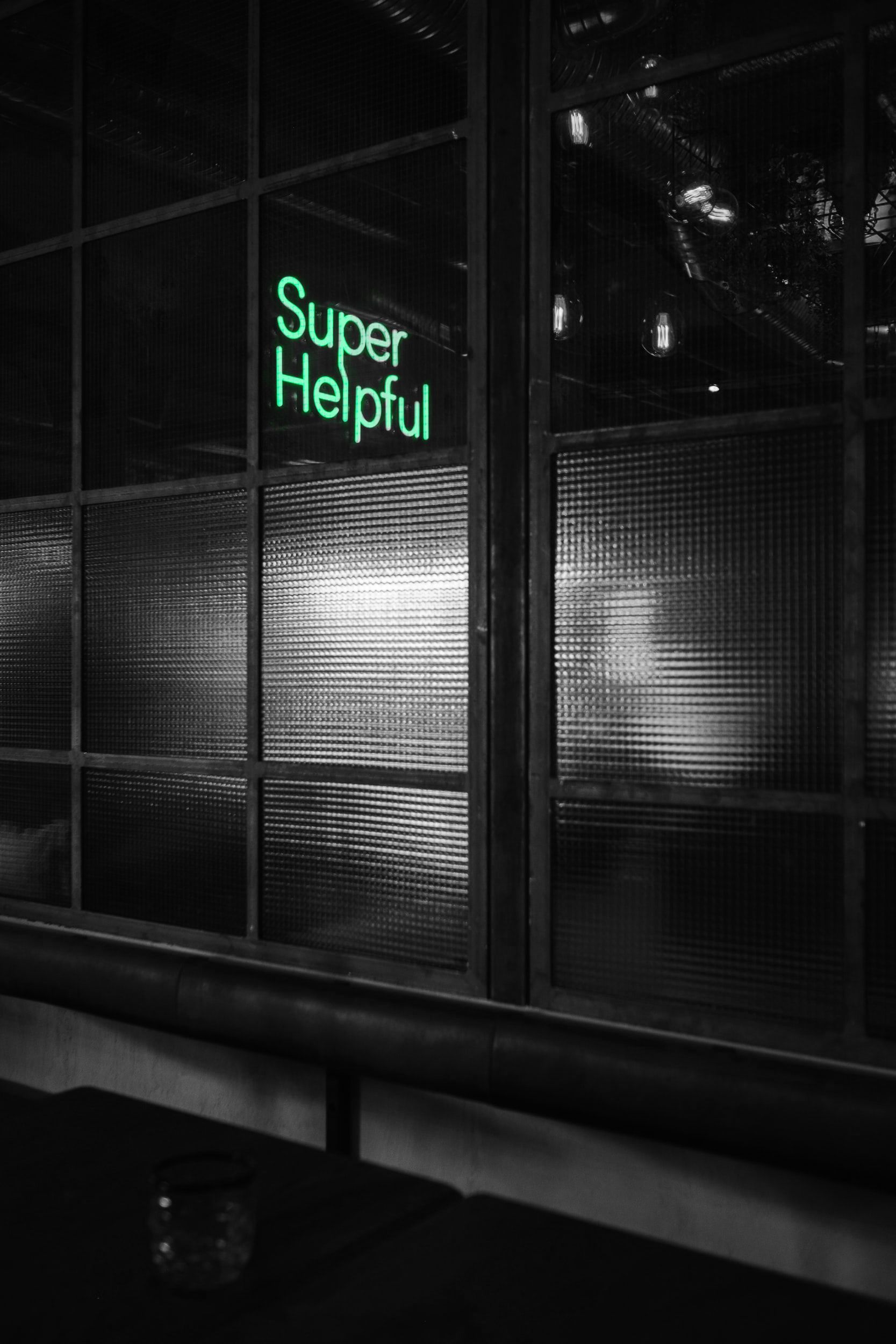 Een zwart-witfoto van een raam met een neonbord waarop staat 'super behulpzaam'