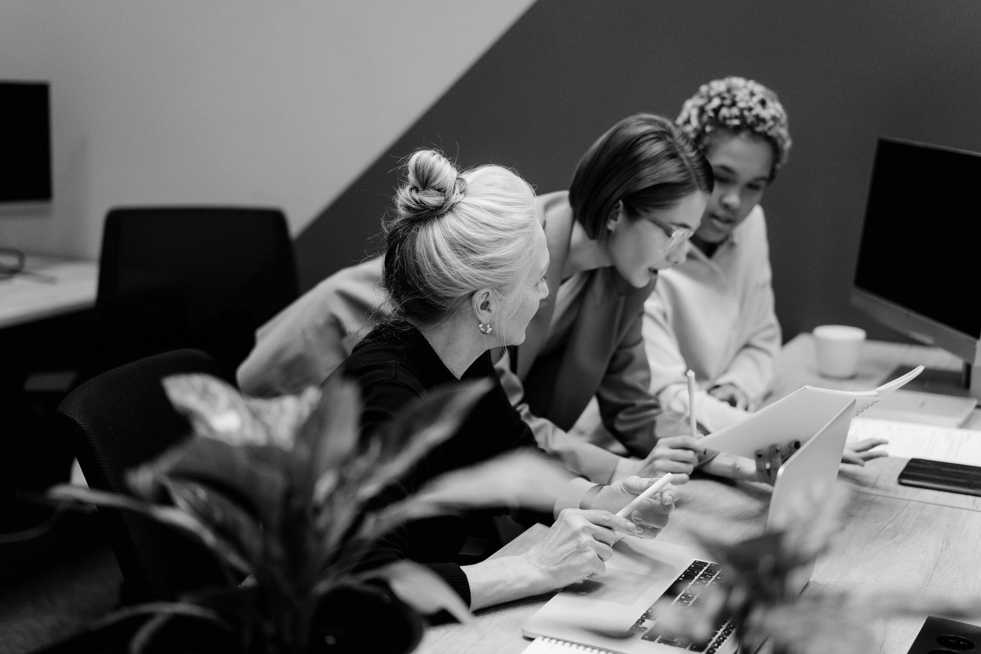 A group of women are sitting at a table looking at a laptop computer.