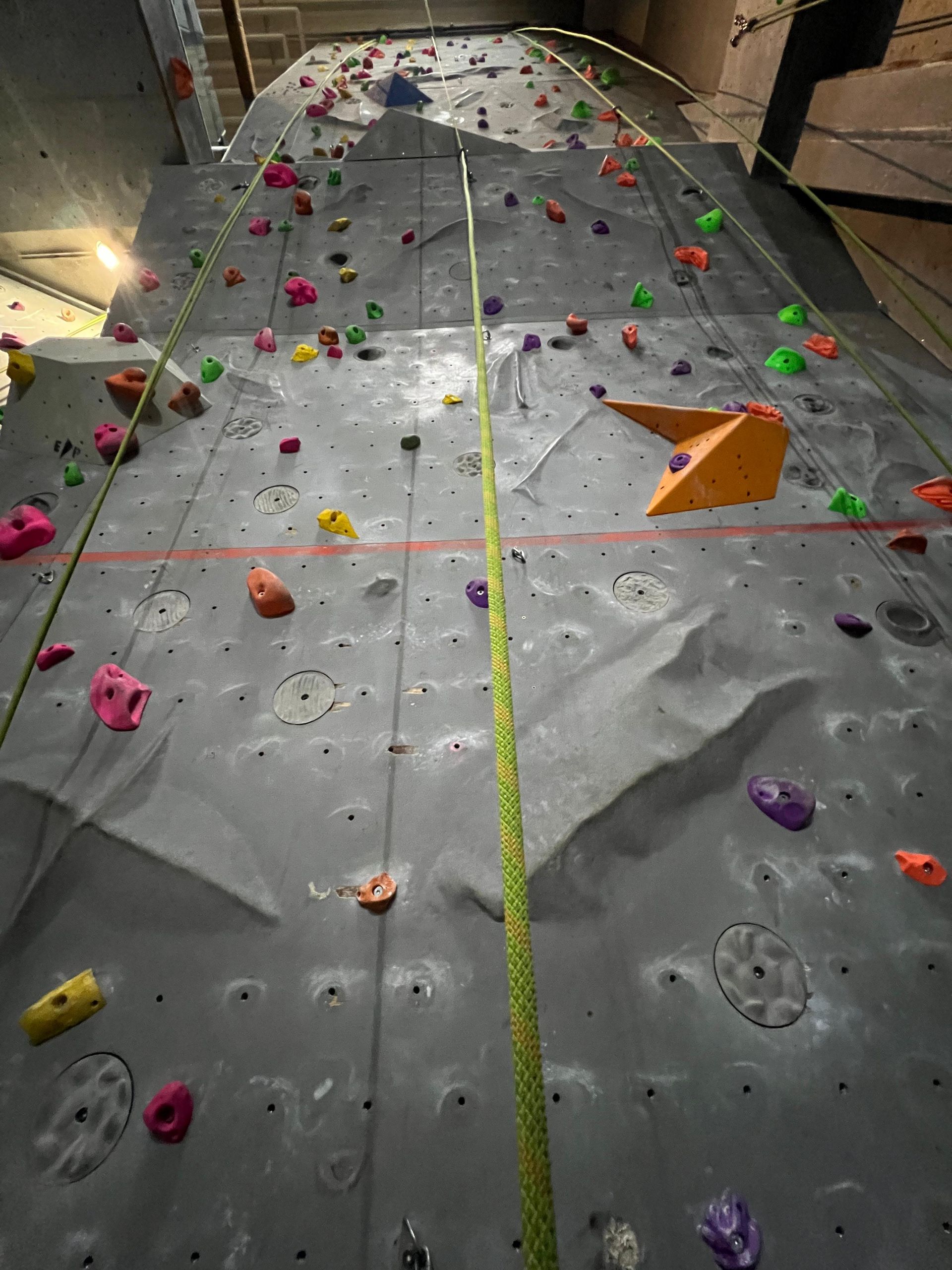 Indoor-Kletterwand mit farbigen Griffen und zwei Kletterseilen, die in der Mitte herunterhängen.