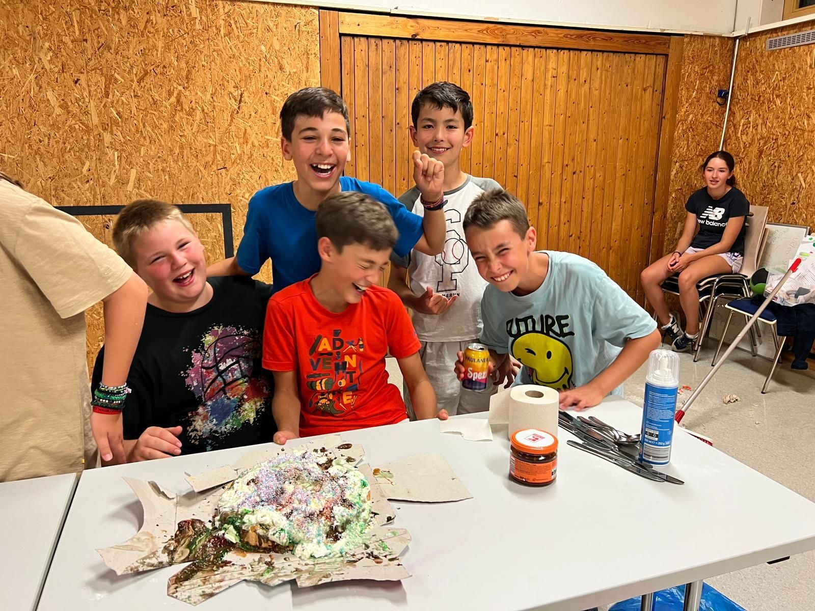 Eine Gruppe junger Jungen sitzt um einen Tisch herum , auf dem ein Kuchen steht.