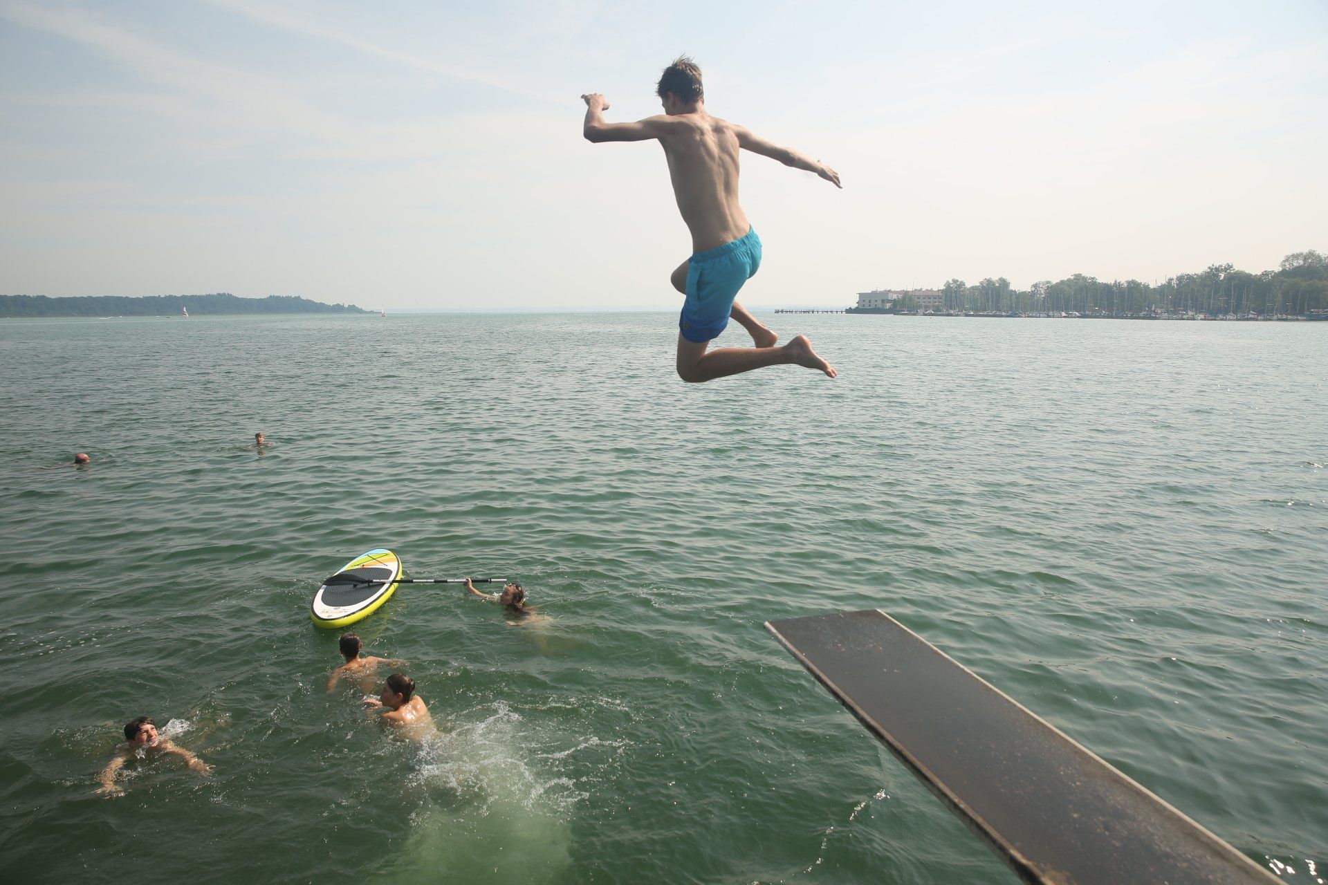 Eine Person springt vom Sprungbrett ins Wasser. Andere Leute schwimmen in der Nähe.