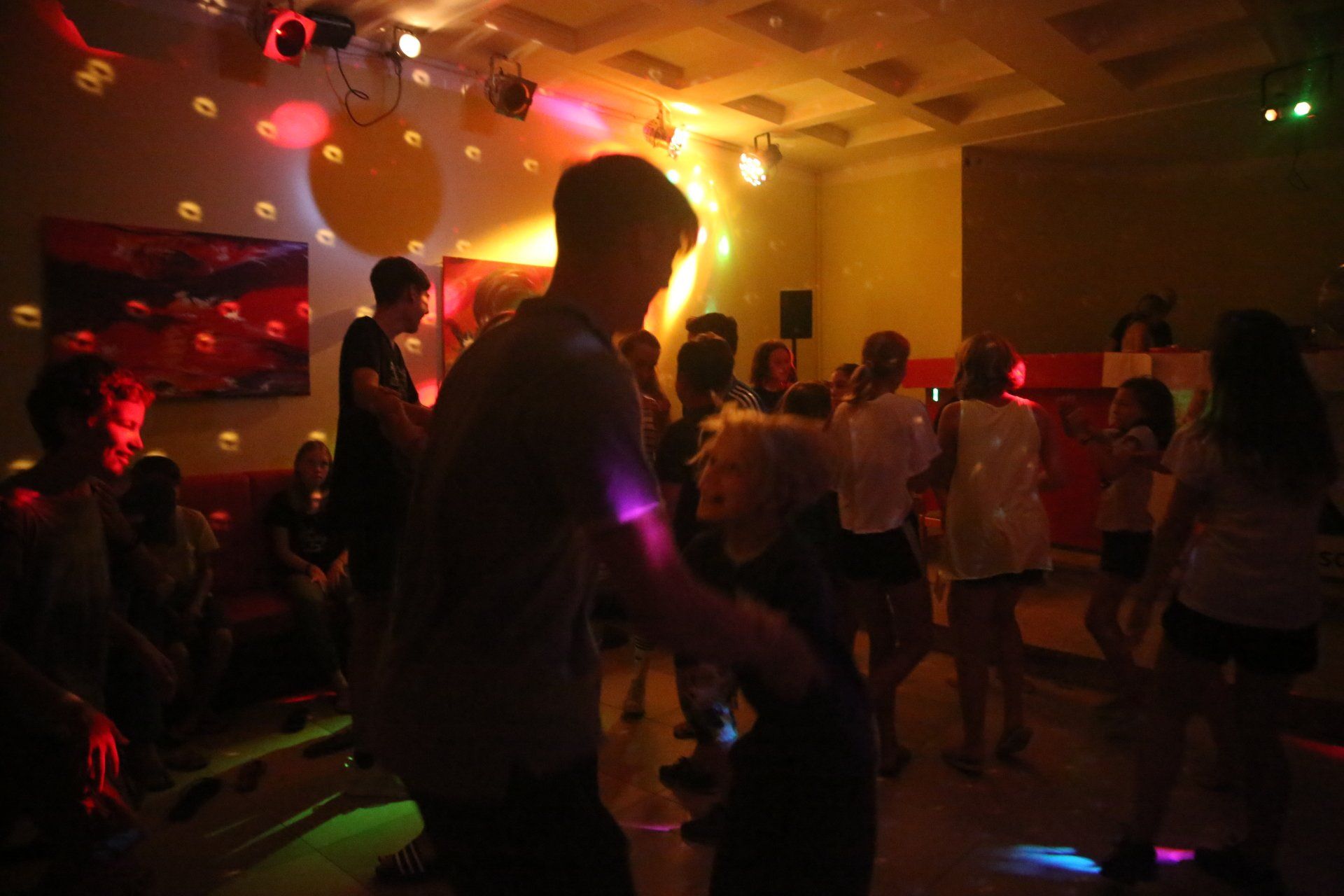 Menschen tanzen in einem hell erleuchteten Raum mit Discokugeln; bunte Lichter erhellen die Szene.