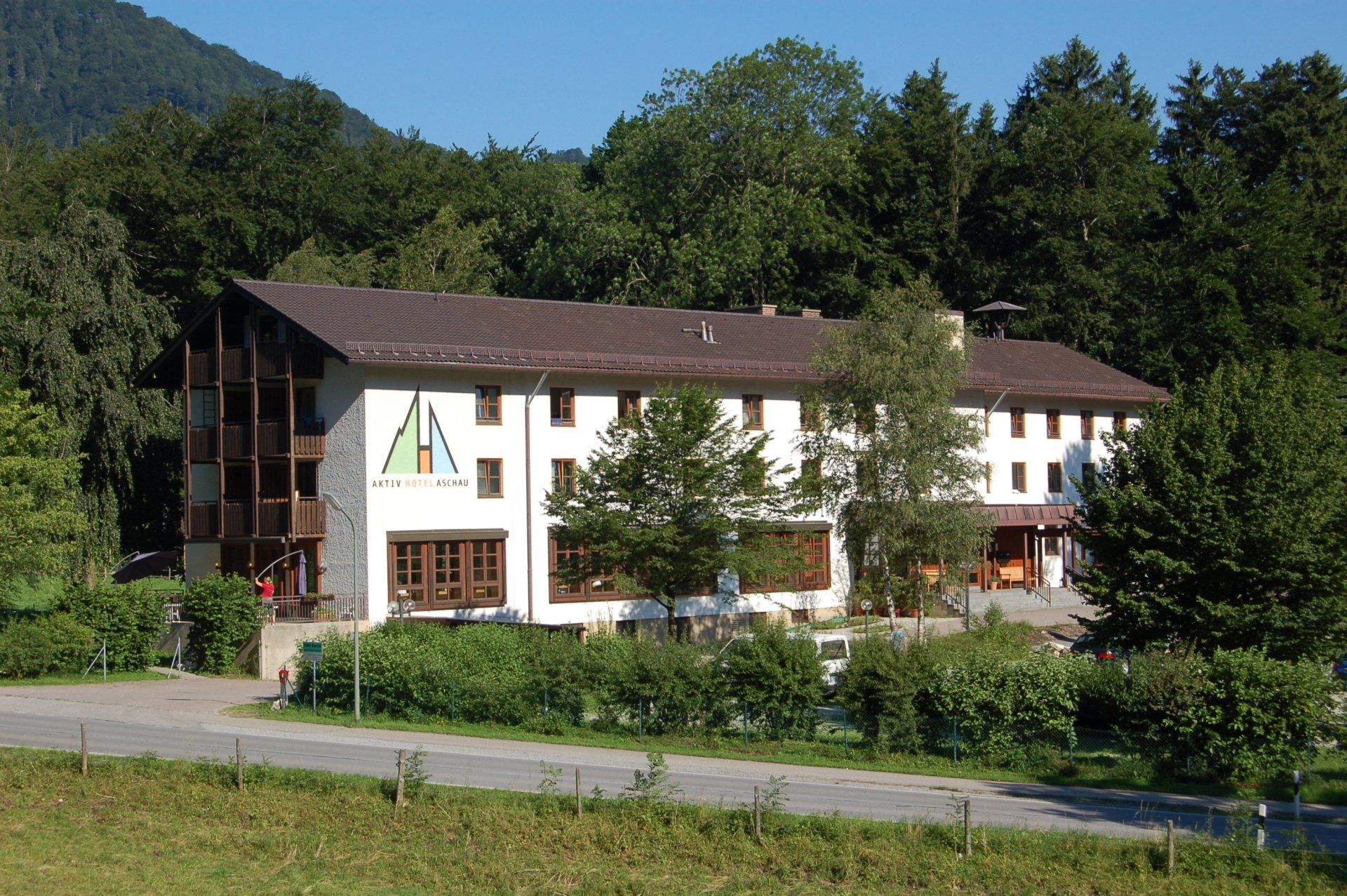 Großes Gebäude mit braunem Dach und weißen Wänden; im Hintergrund Bäume.
