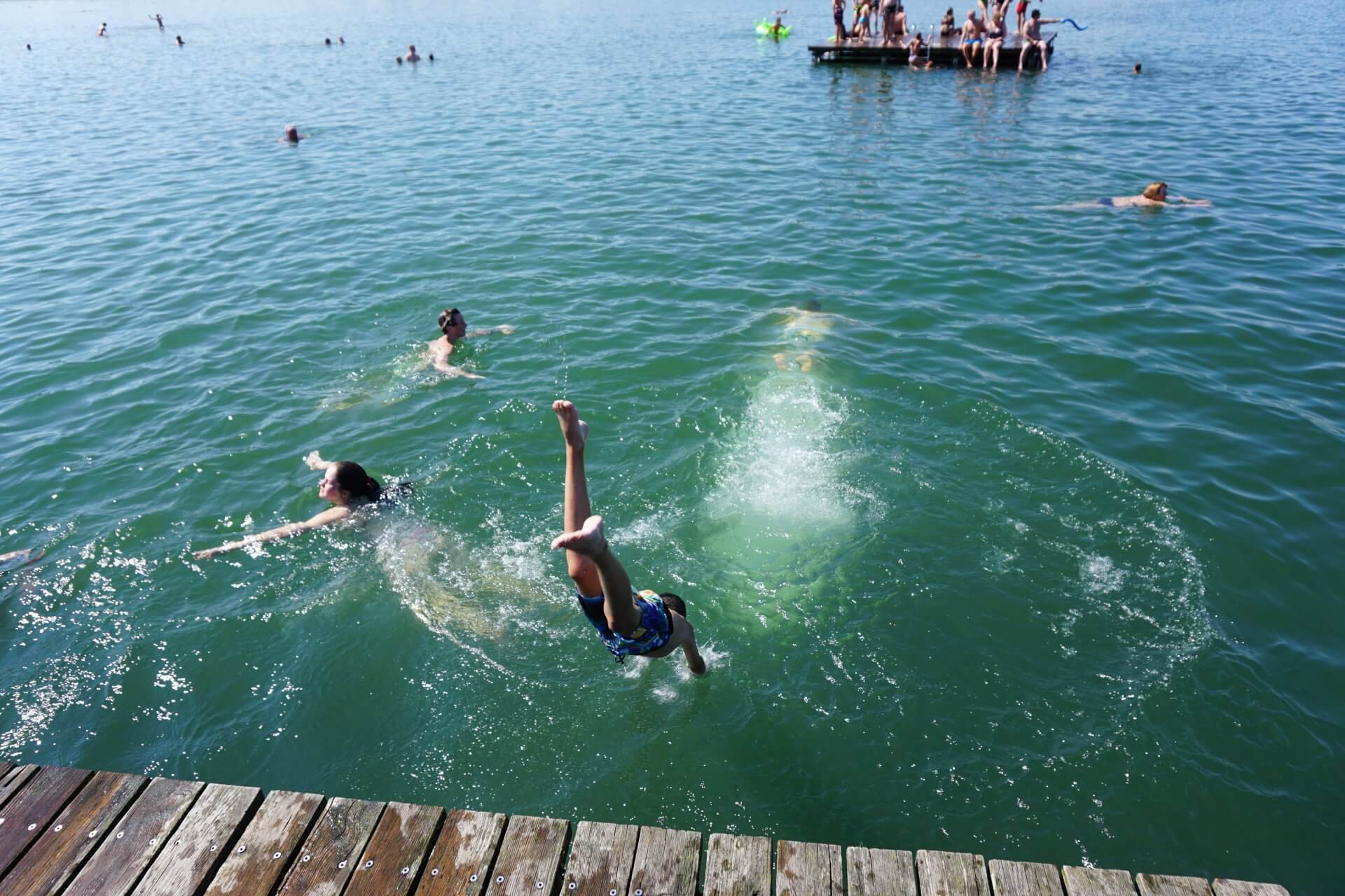Menschen schwimmen und springen von einem Holzsteg in einen See.