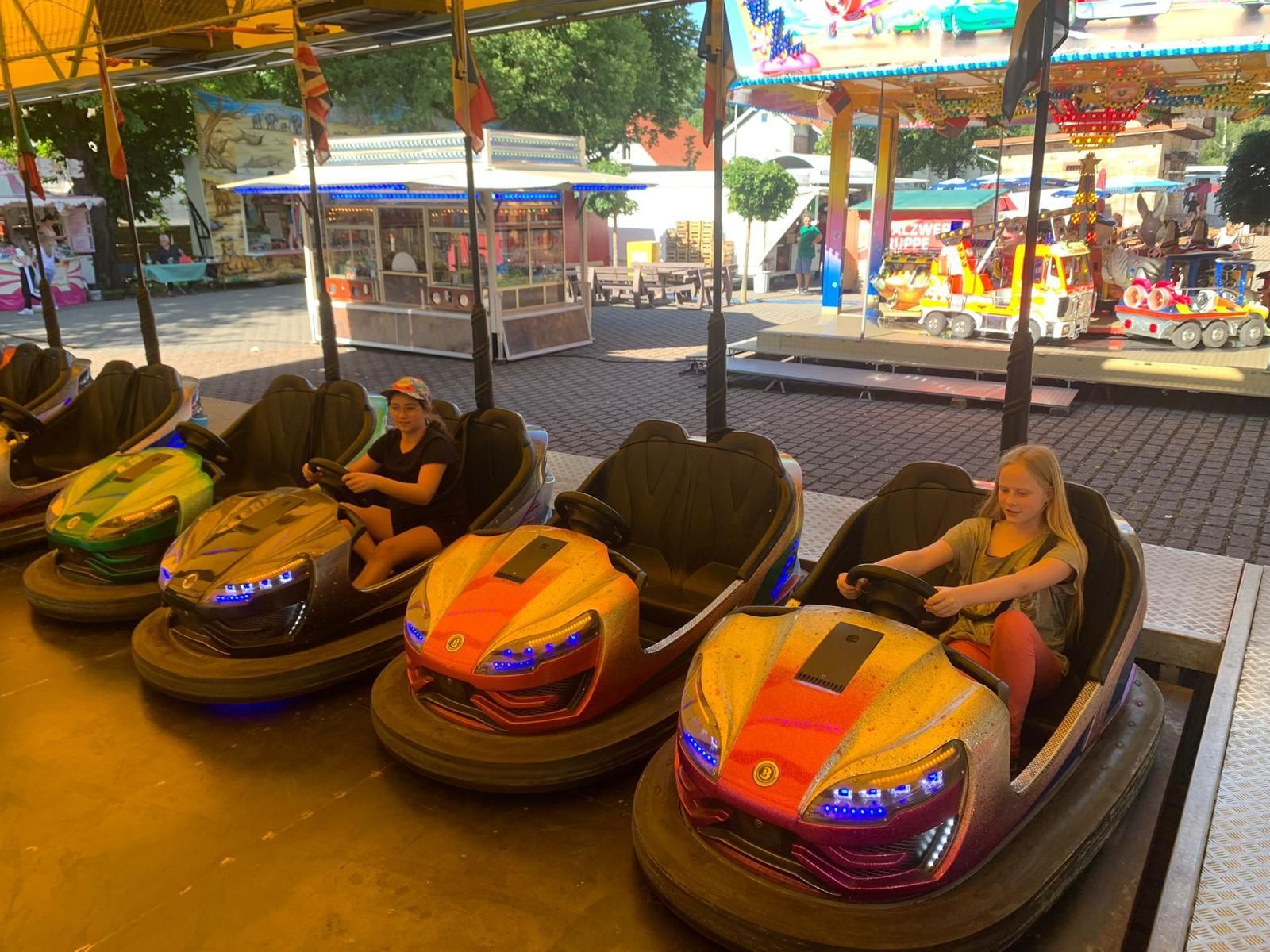 Kinder in bunten Autoscootern in einem Vergnügungspark, die herumfahren und lächeln.