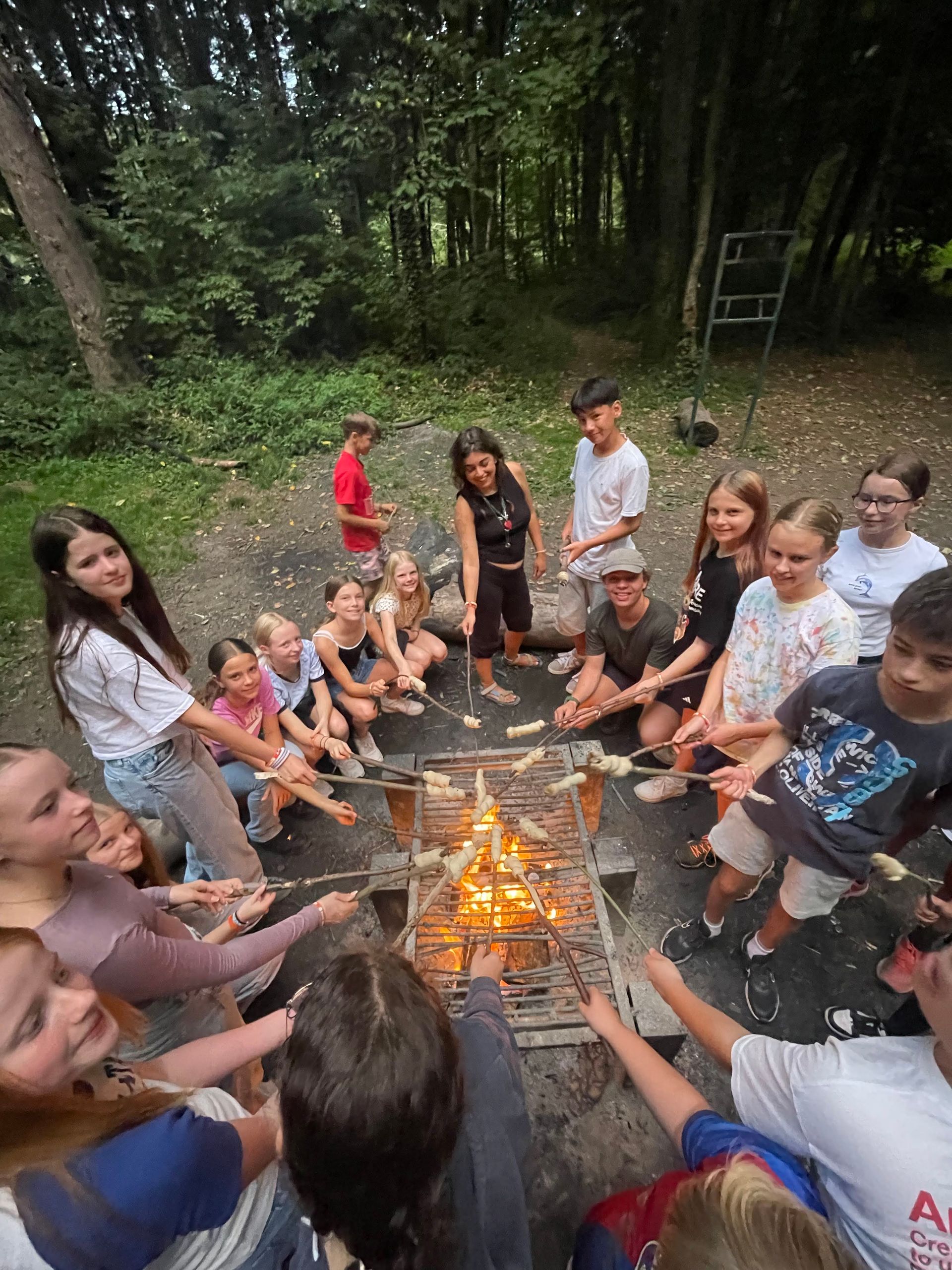 Eine Gruppe Kinder röstet Essen über einer Feuerstelle in einem Waldgebiet.