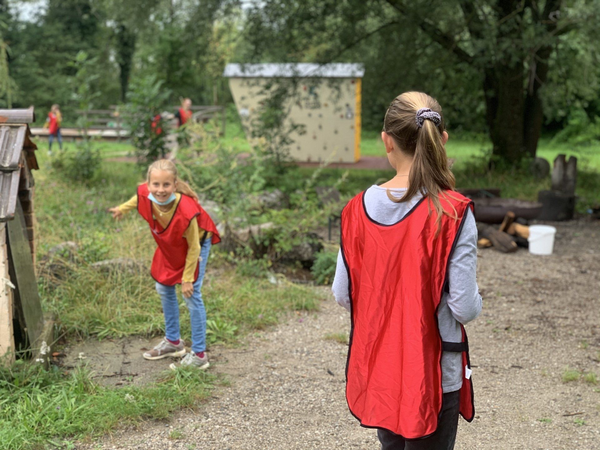 Zwei Kinder in roten Westen spielen draußen in der Nähe eines Baches; eines zeigt mit dem Finger, das andere schaut zu.