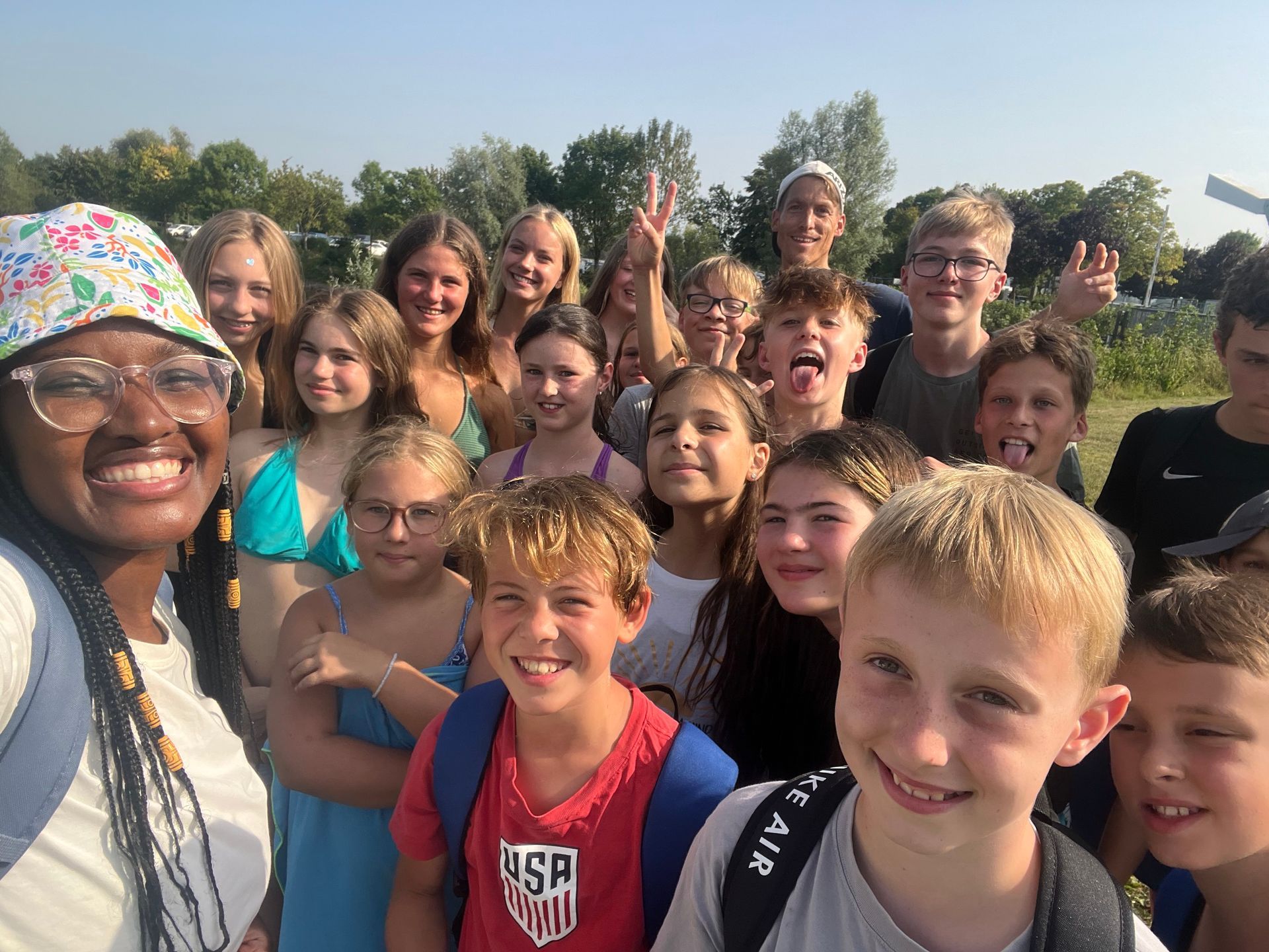 Eine Gruppe lächelnder Kinder und ein Erwachsener posieren im Freien für ein Selfie.
