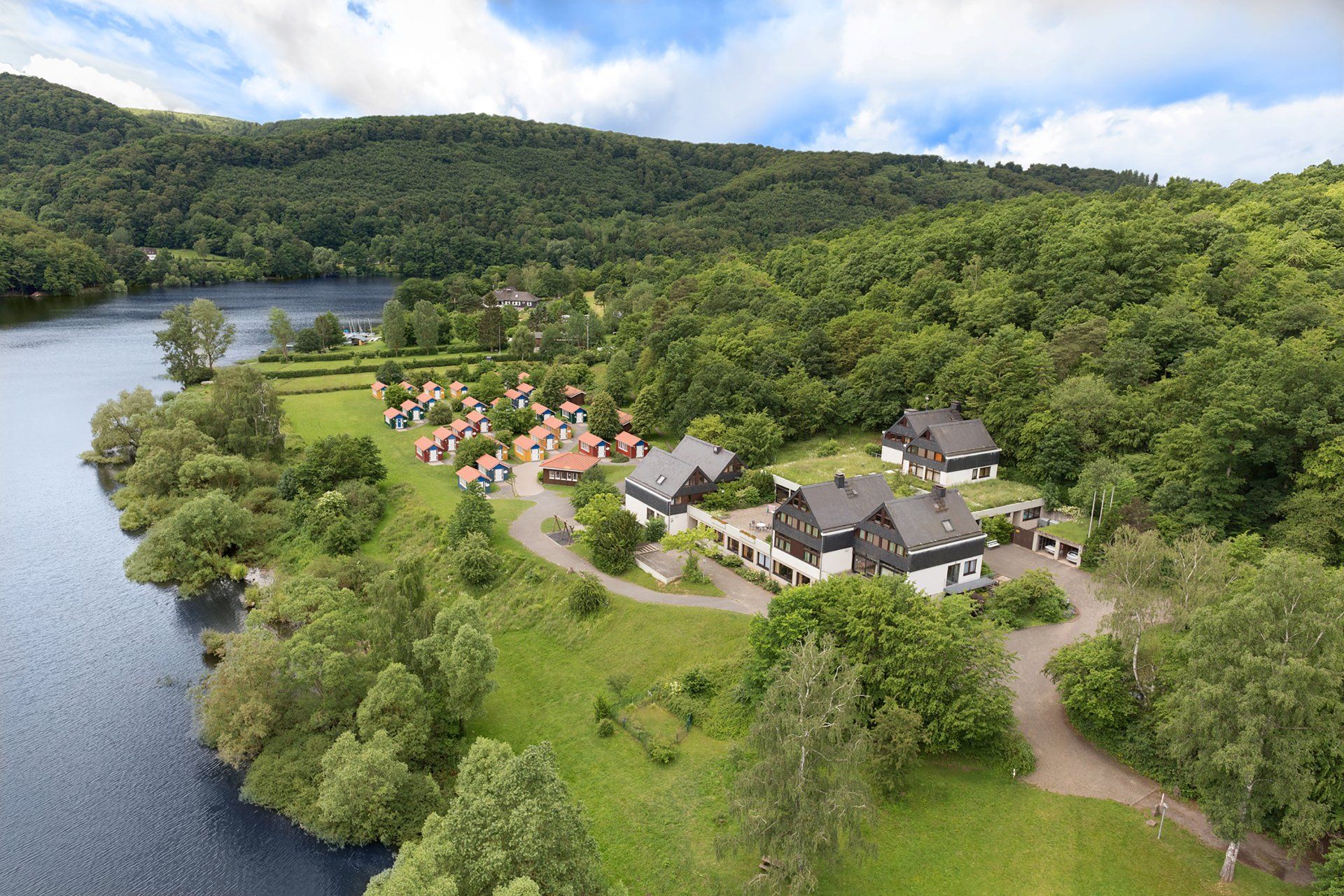 Seeuferresort mit zahlreichen Hütten und Häusern, eingebettet in üppig grüne Bäume unter einem bewölkten Himmel.