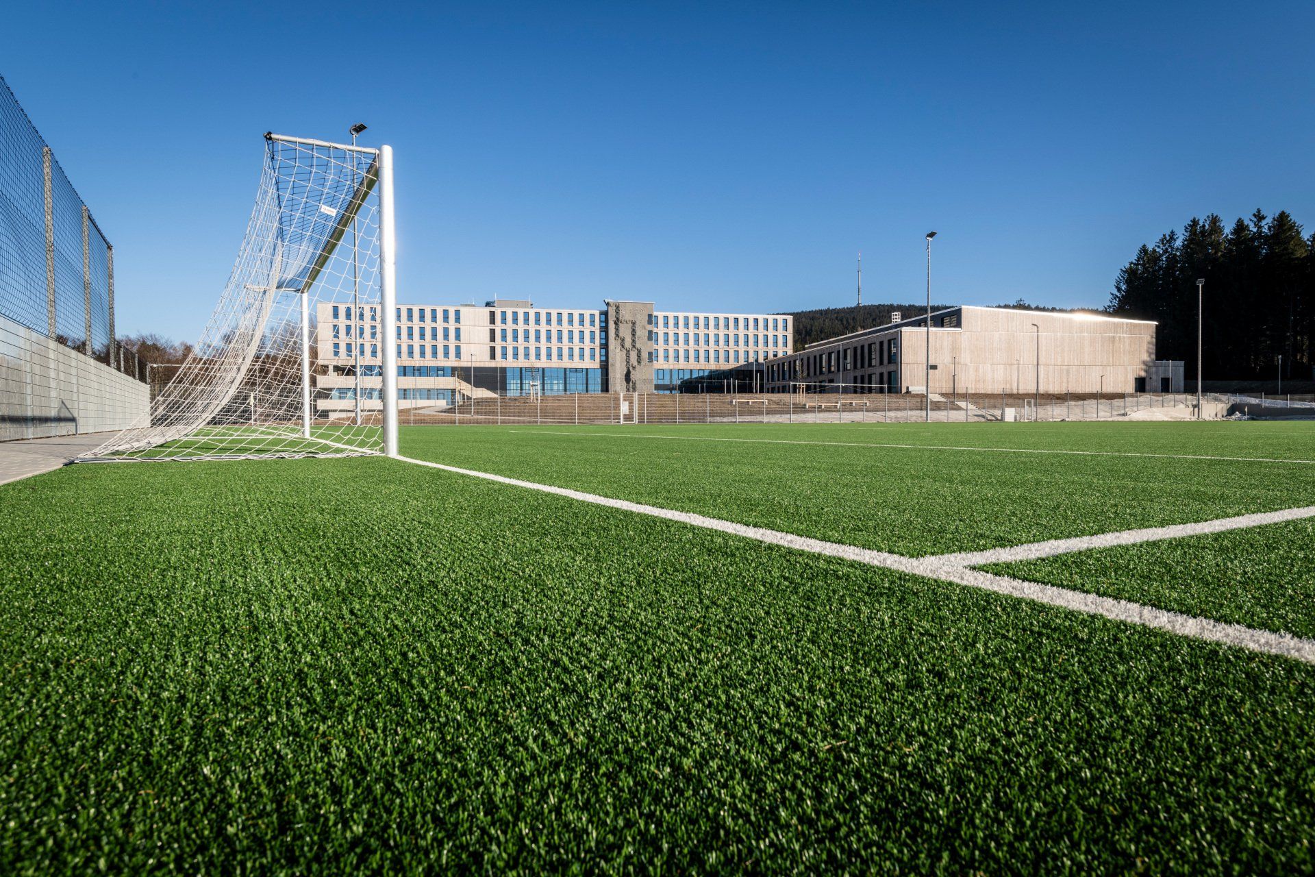 Fußballfeld mit Tor und Gebäude im Hintergrund an einem sonnigen Tag.