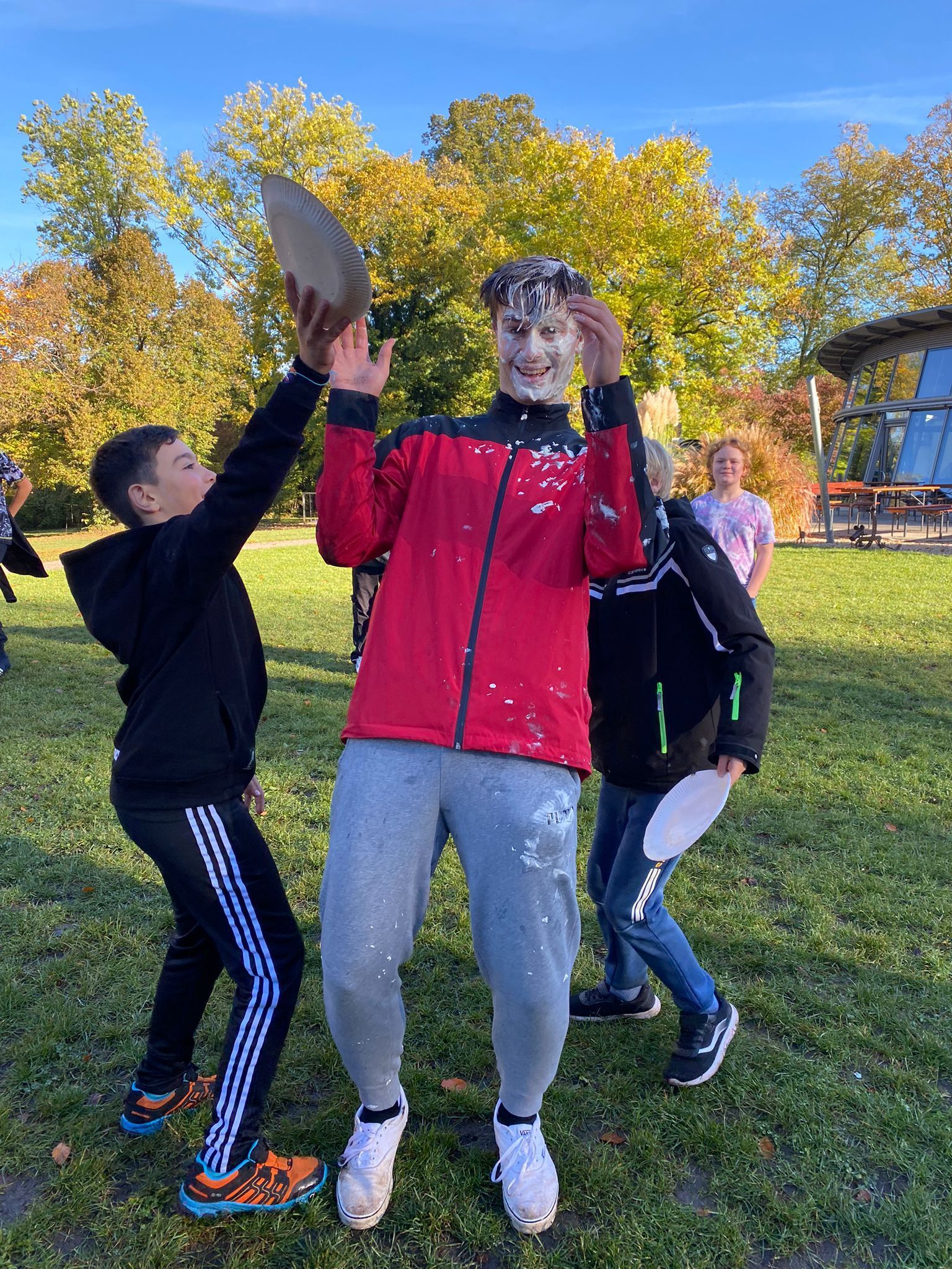 Eine Gruppe junger Jungen steht mit einem mit Kuchen bedeckten Mann auf einem Feld.