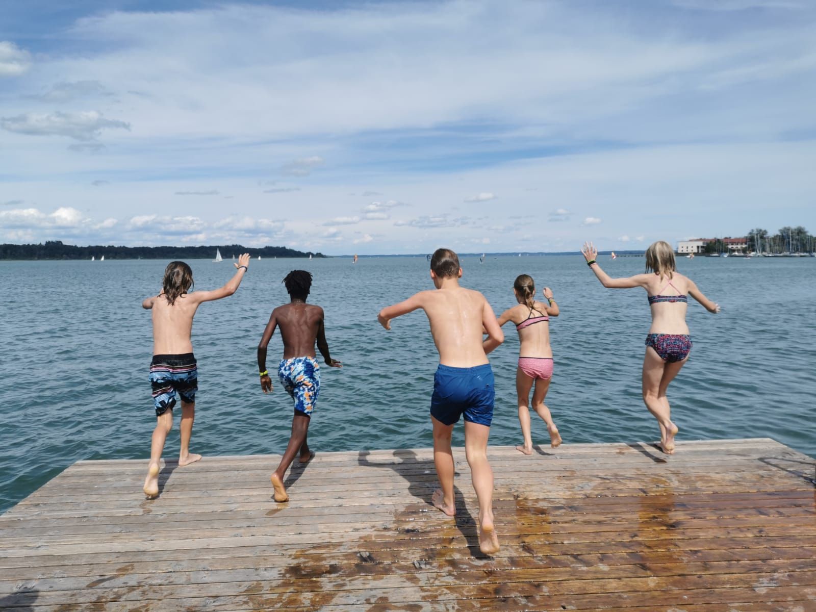 Eine Gruppe Kinder springt von einem Steg ins Wasser.