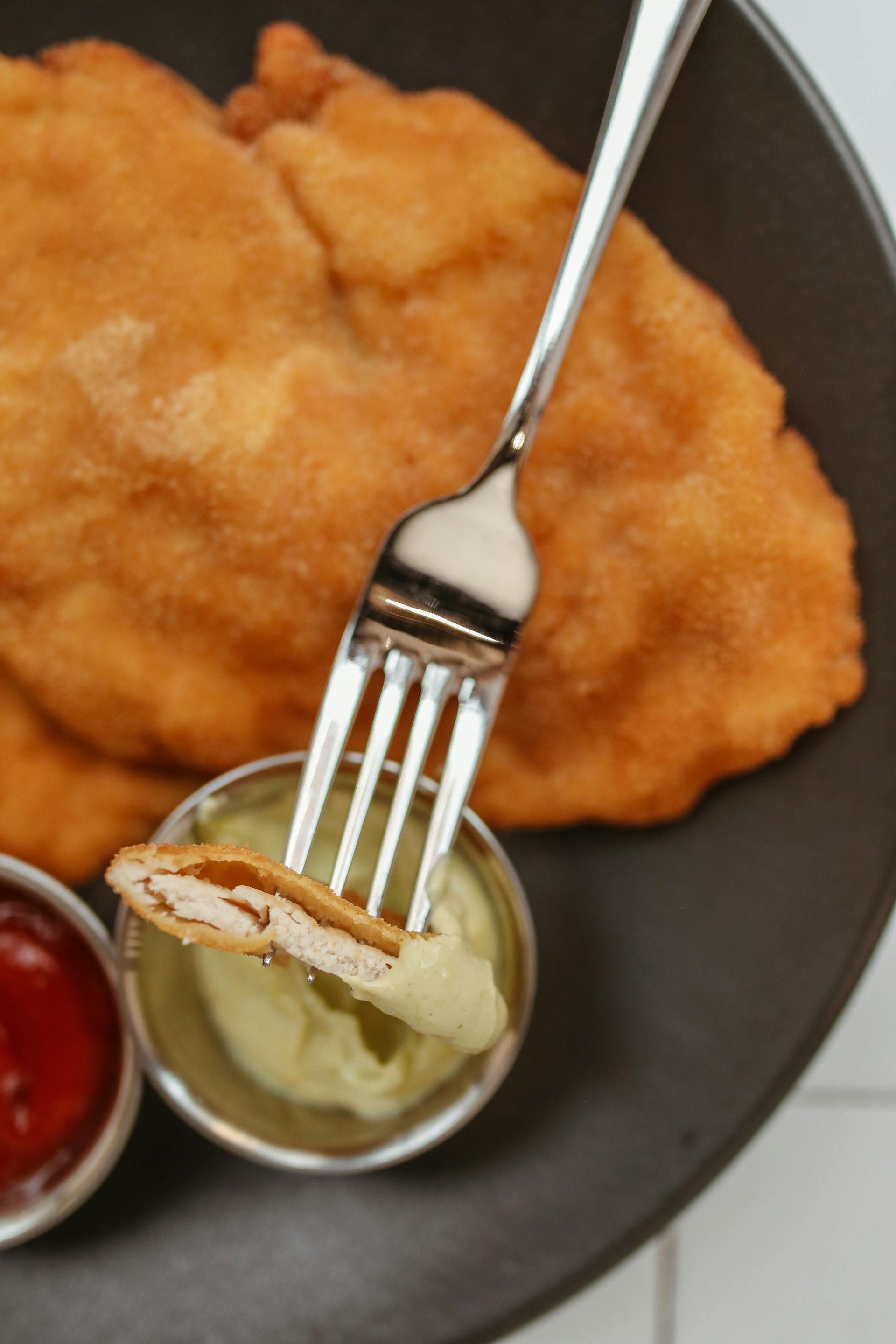Schnitzel auf einem Teller mit Ketchup, Senf und einer Gabel, die einen Bissen hält.