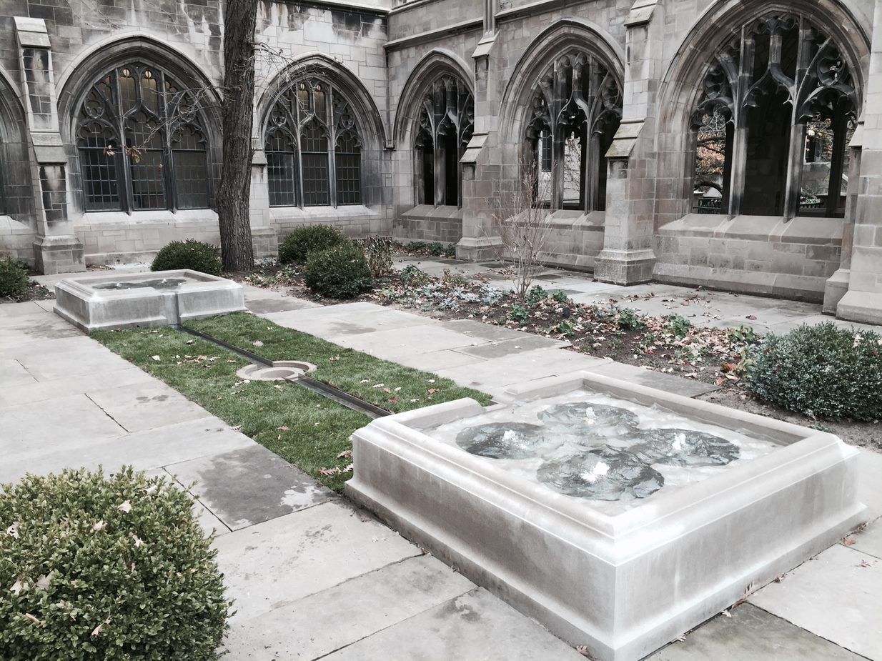 A black and white photo of a church courtyard with a fountain in the middle.