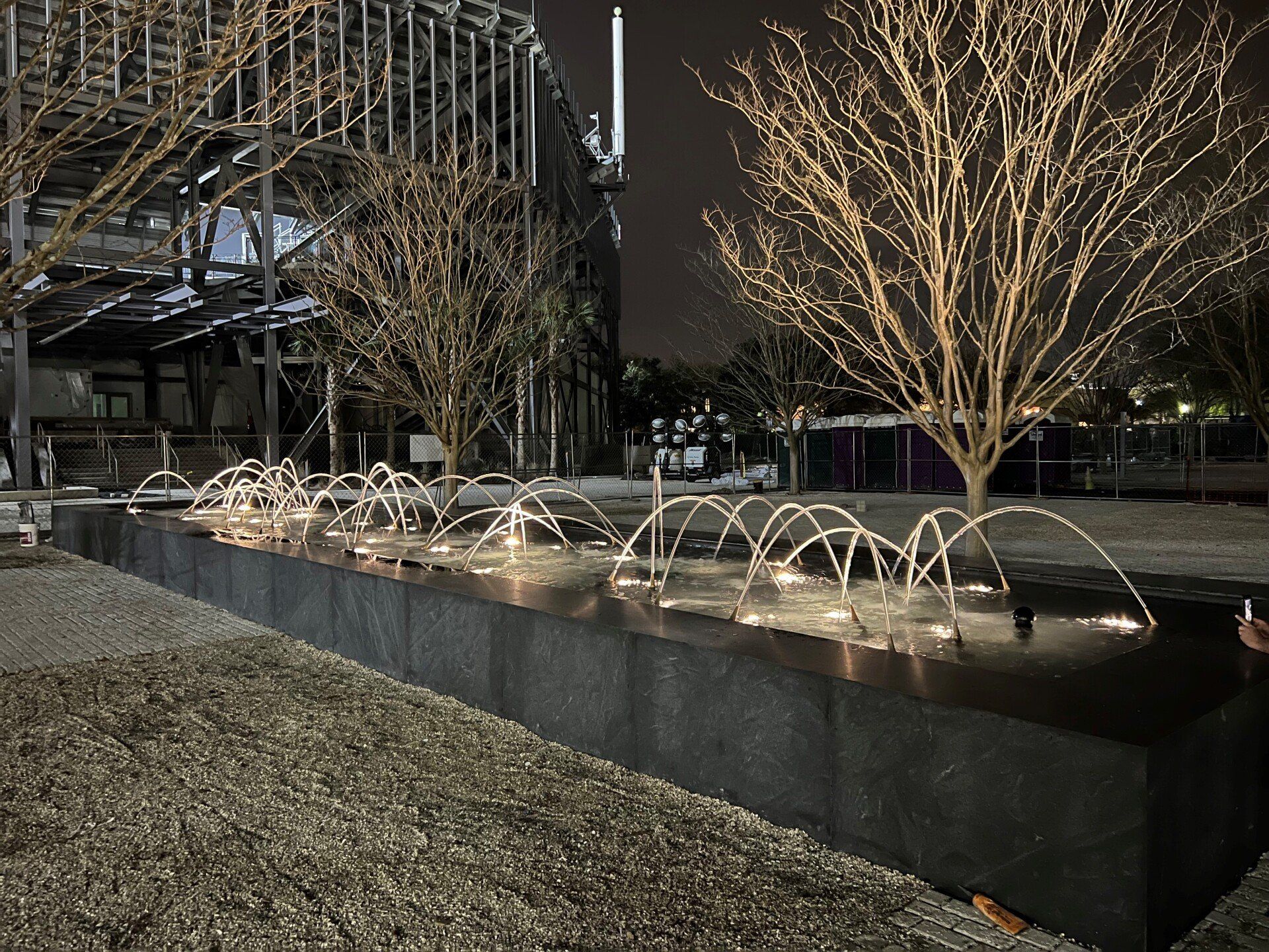A fountain in a park at night with trees in the background.