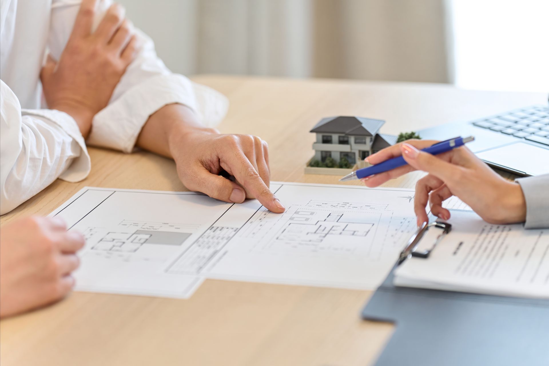 Hands reviewing house plans at a table with a small model home and blueprints