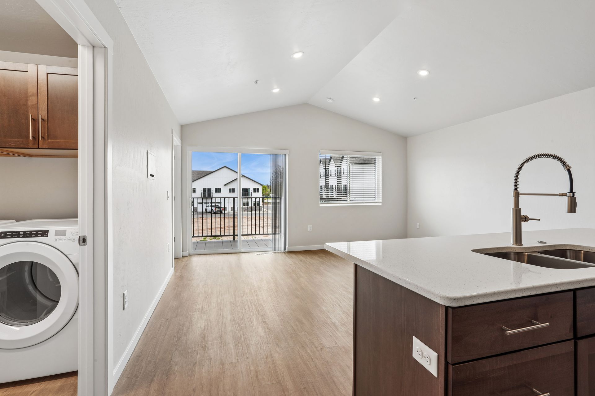 Bright open kitchen and living area with island, laundry closet, and sliding doors to a balcony.