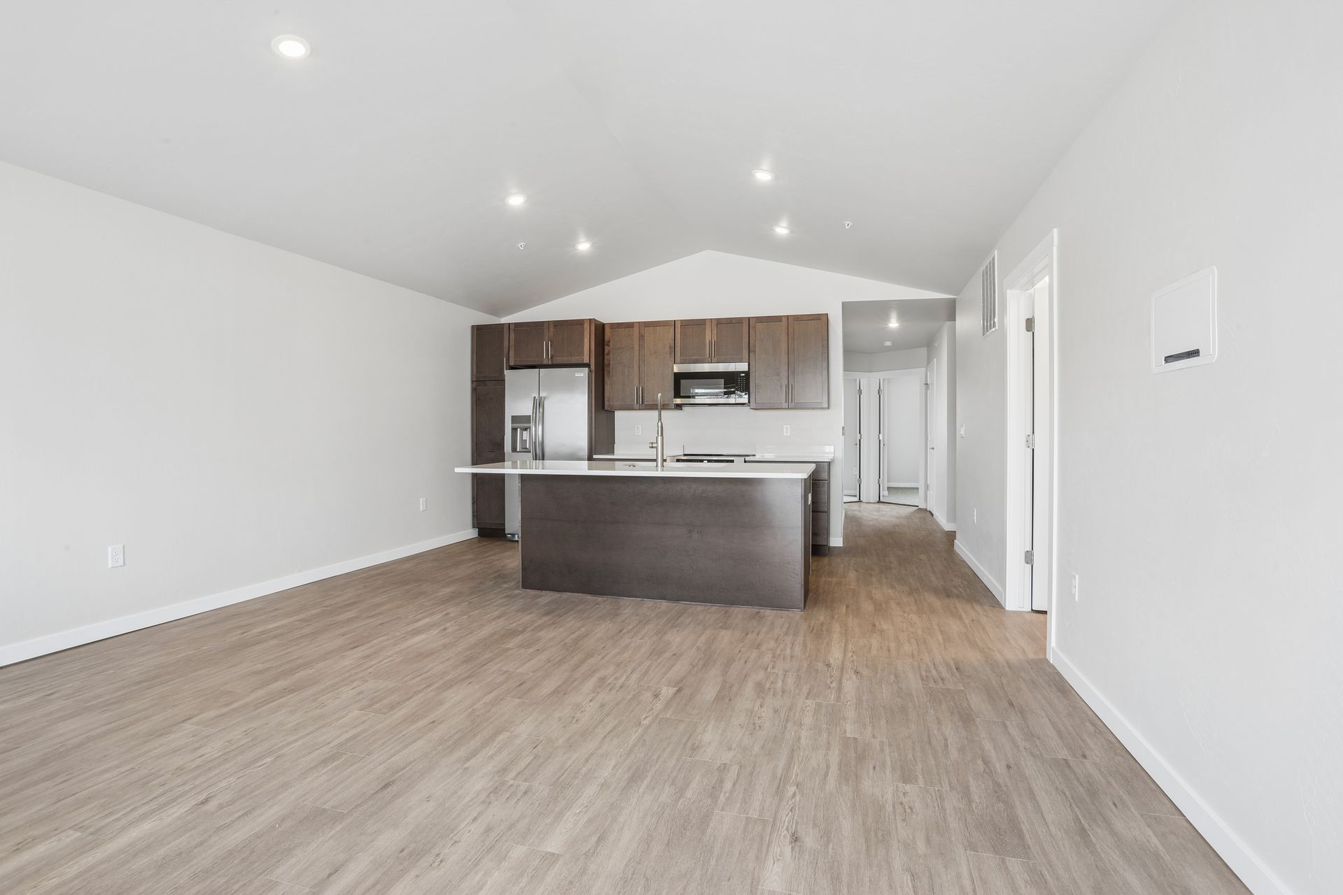 Open-plan kitchen and living area with light wood floors, white walls, and dark cabinets.