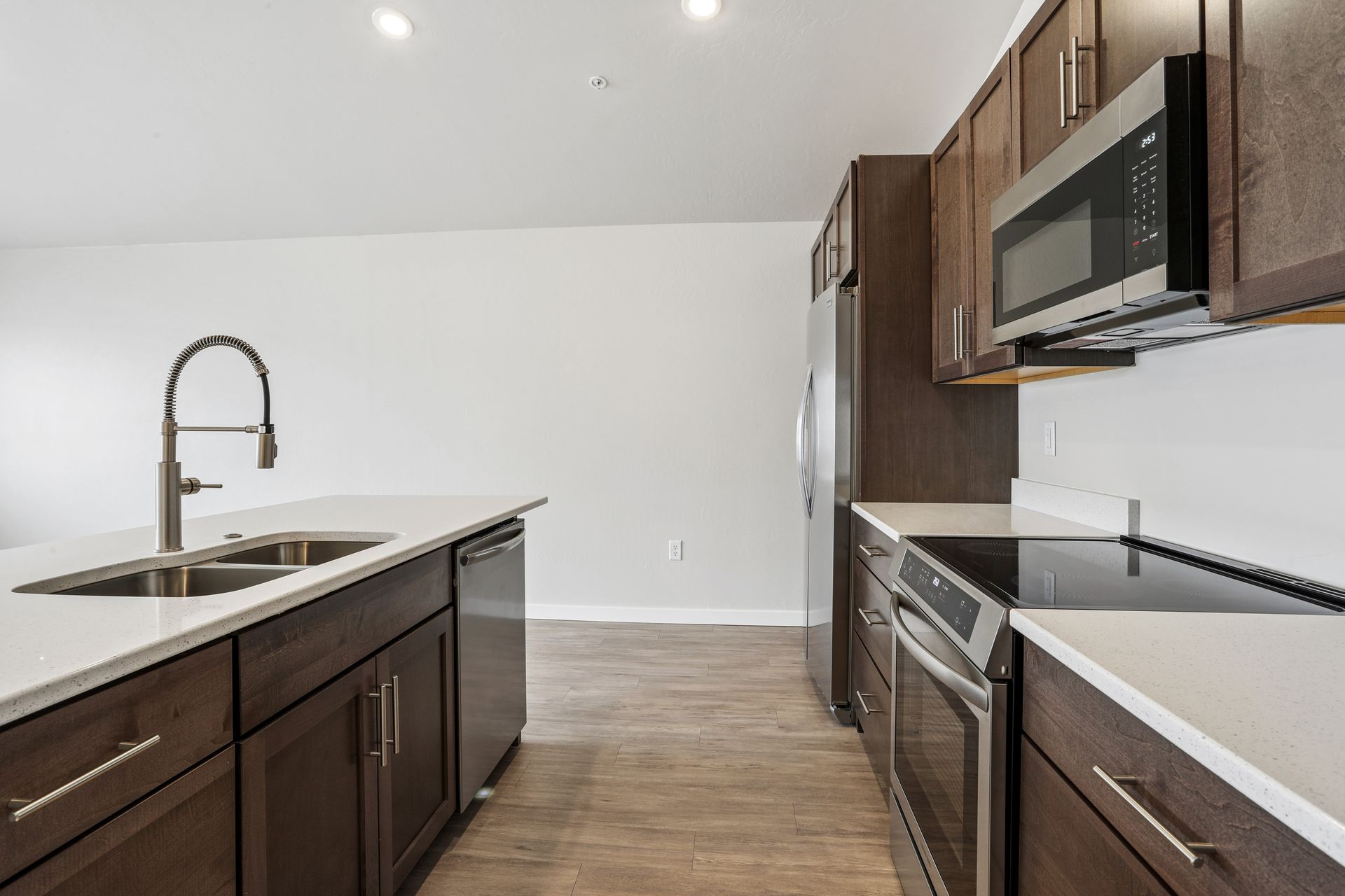 Modern kitchen with dark wood cabinets, white countertops, stainless steel appliances, and an island sink.