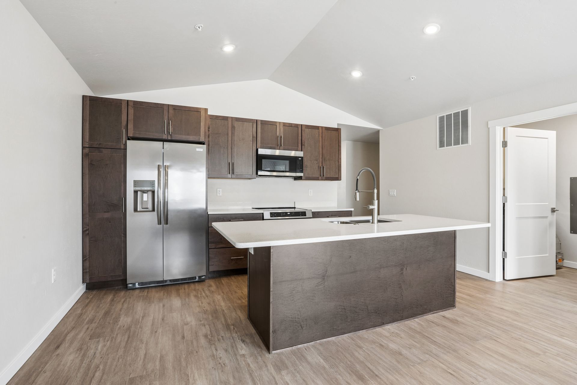 Modern kitchen with stainless steel appliances, dark cabinets, and a large island with white countertop