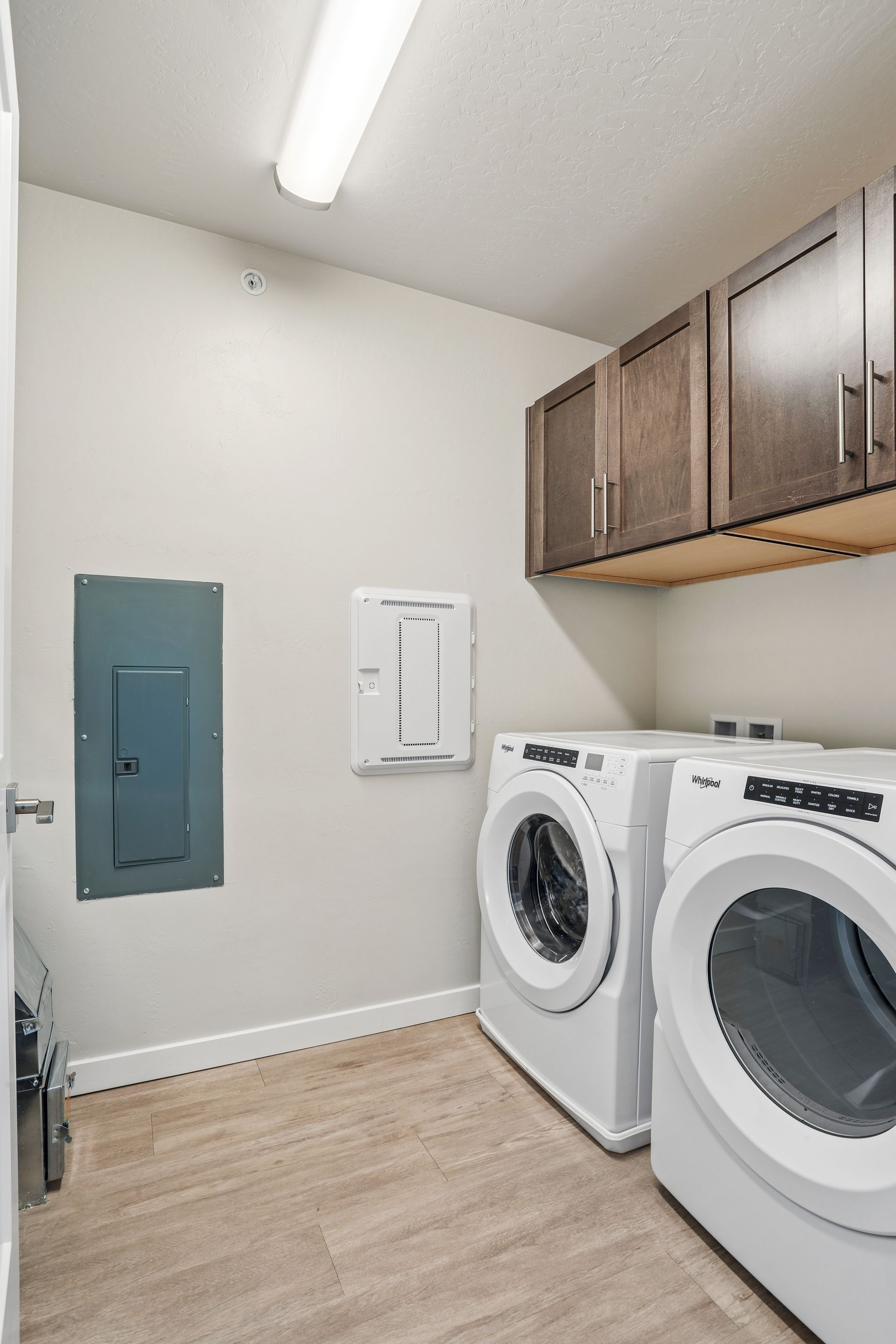 Laundry room with washer, dryer, overhead cabinets, and a utility panel on the wall.