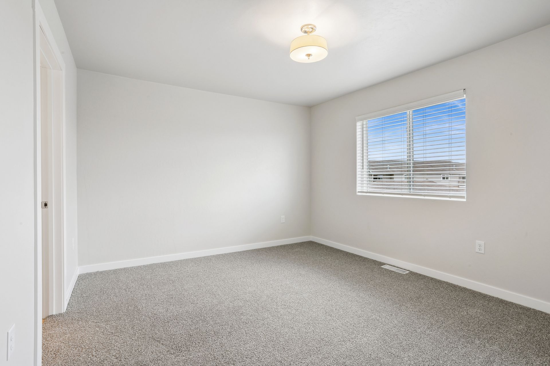Empty white bedroom with gray carpet and a window letting in daylight