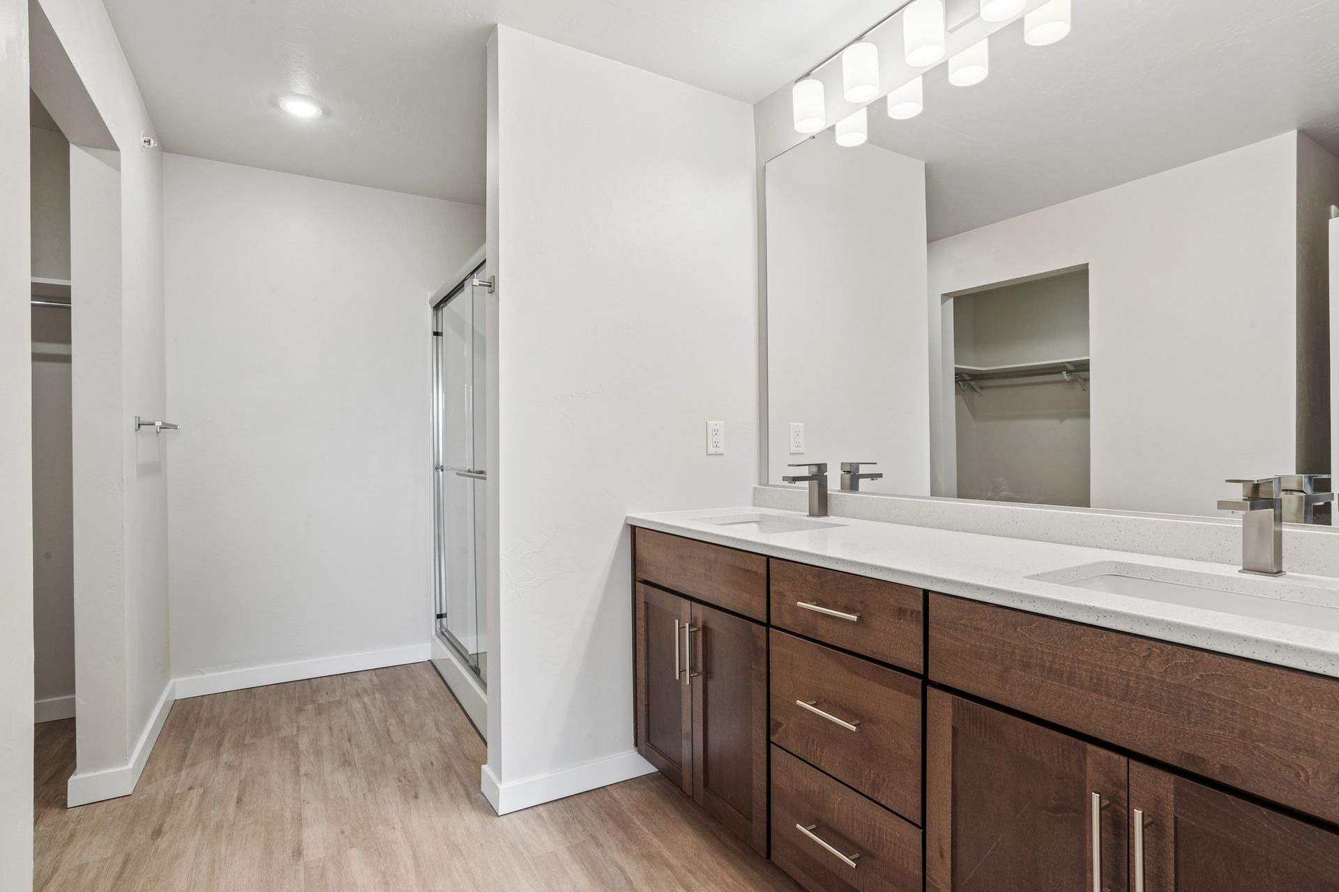 Bright bathroom with double vanity, dark wood cabinets, white walls, and light wood flooring.